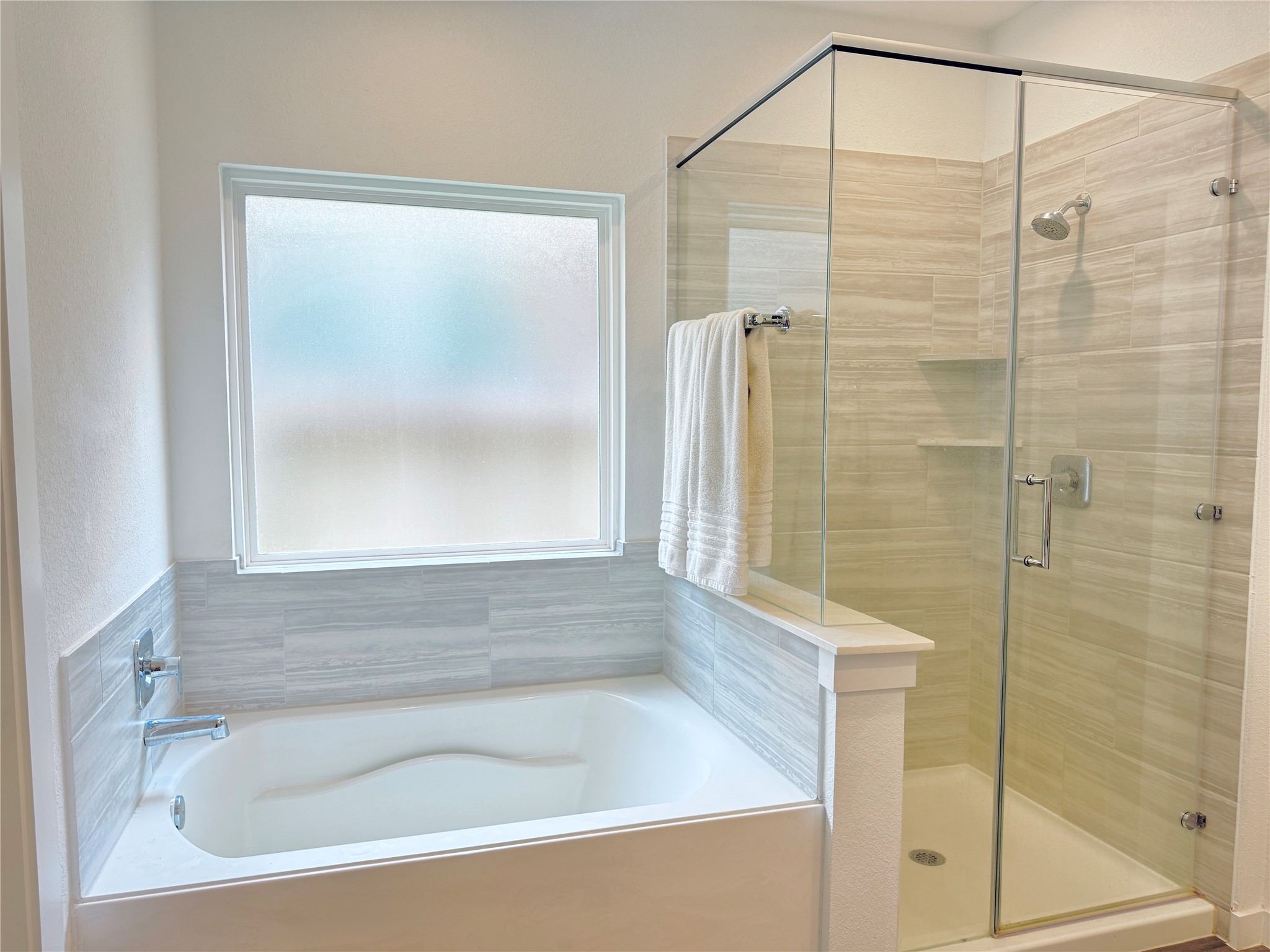 Elegant bathroom with a luxurious soaking tub and a modern glass-enclosed shower, complemented by stylish tilework and natural light from a frosted window
