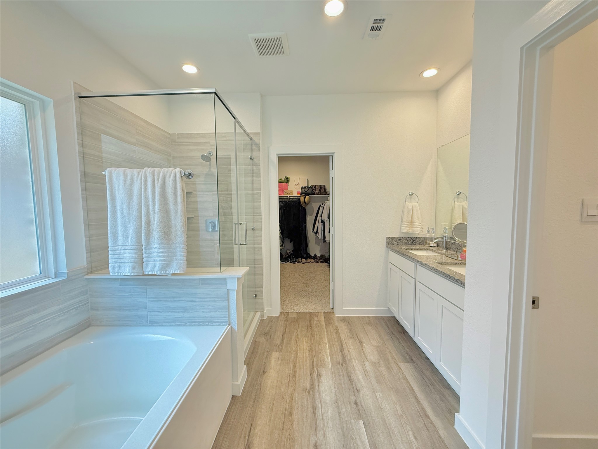 Primary bathroom featuring a luxurious soaking tub, spacious glass-enclosed shower, dual vanity with granite countertops, and a walk-in closet