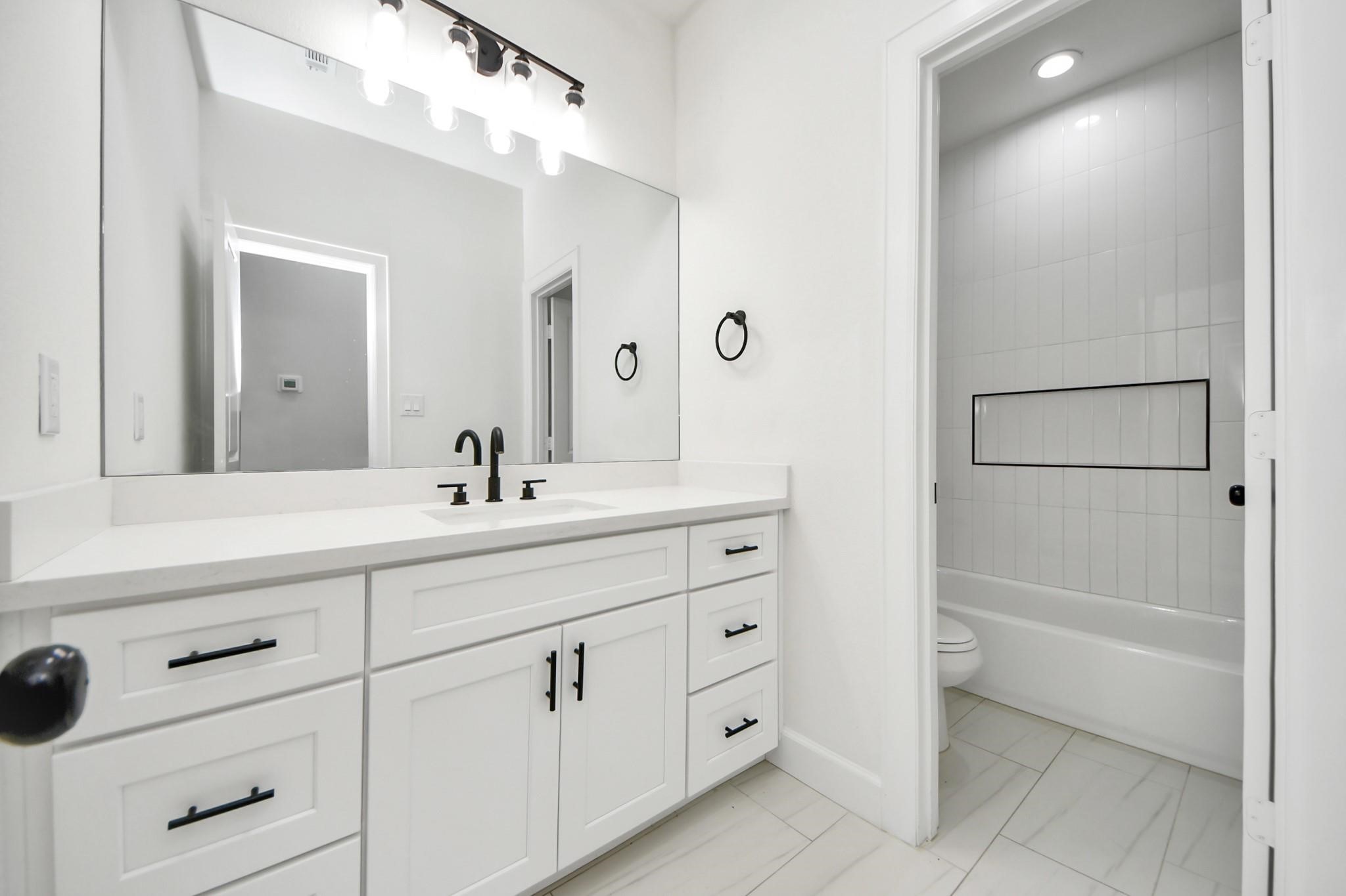 This full bathroom features a quartz-topped vanity, designer black hardware, and ample under-sink storage.