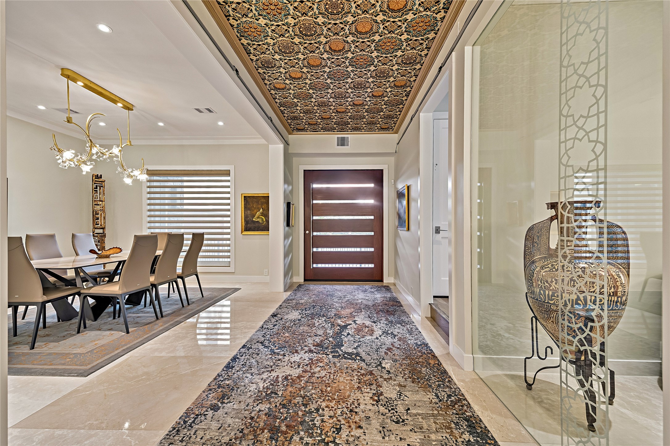 An impressive view through the entrance gallery showcasing elaborate ceiling artistry, sophisticated lighting, and the elegant formal dining room. The open architectural arrangement creates a seamless transition between the home's principal gathering areas.
