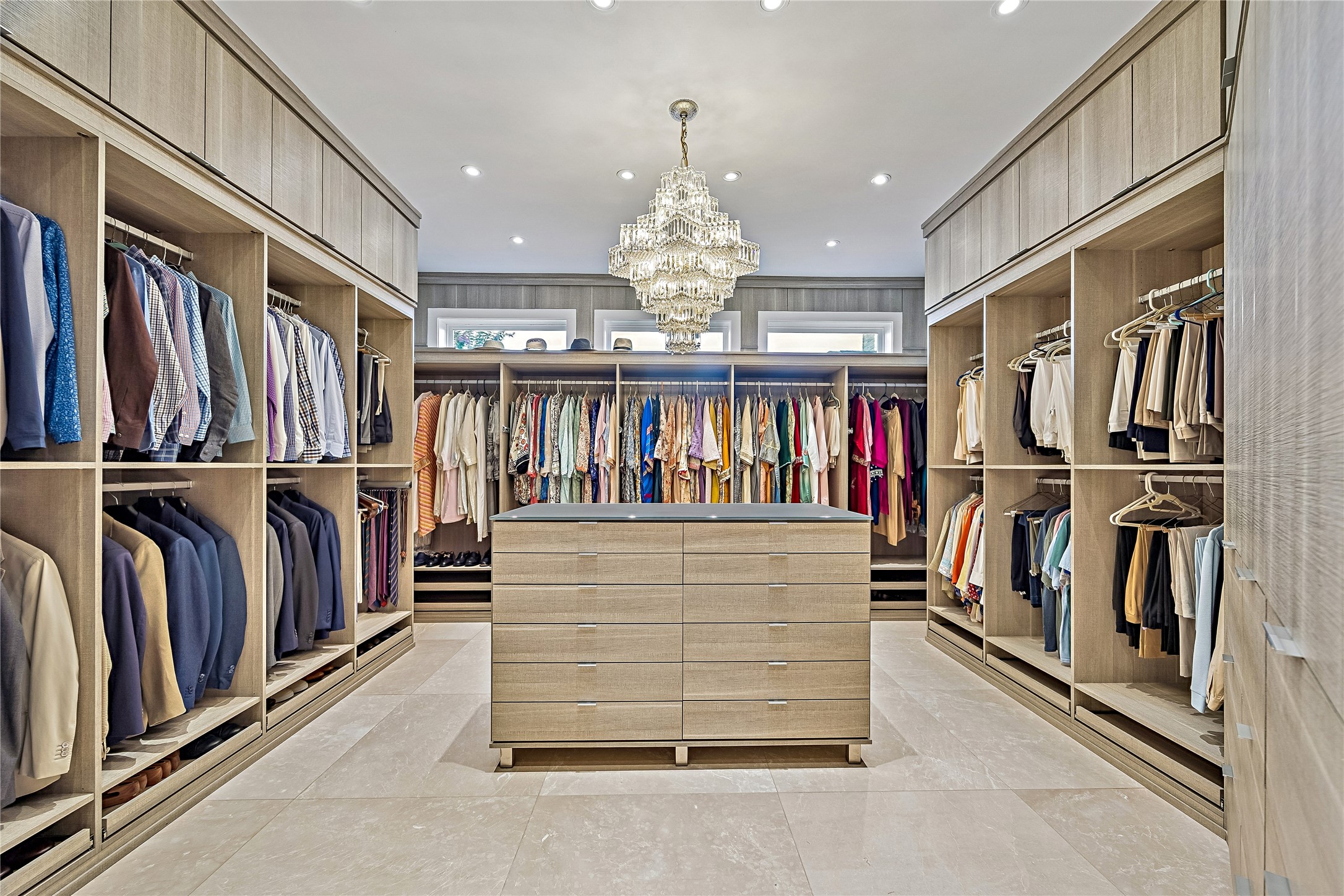 An extraordinary walk-in closet featuring extensive custom shelving, built-in hanging areas, a center storage island, and an elegant chandelier. Designed to accommodate a substantial wardrobe with beautifully organized storage.