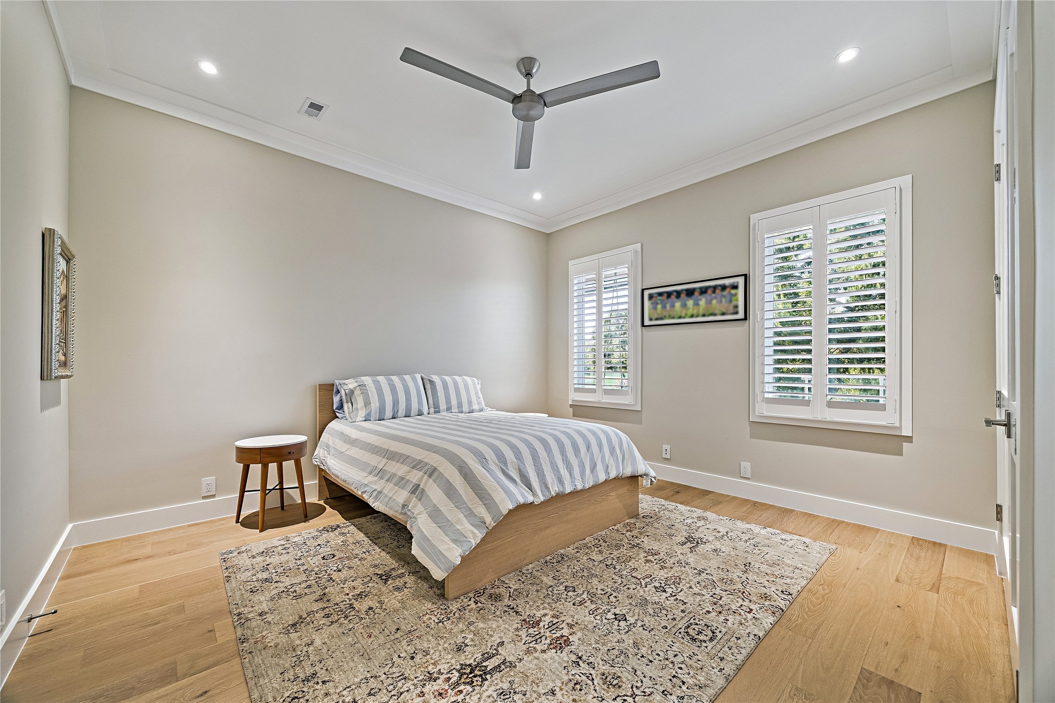 Spacious upstairs guest bedroom showcasing neutral walls, wood flooring, and multiple windows that fill the room with natural light. The home's upper level offers generously sized accommodations.