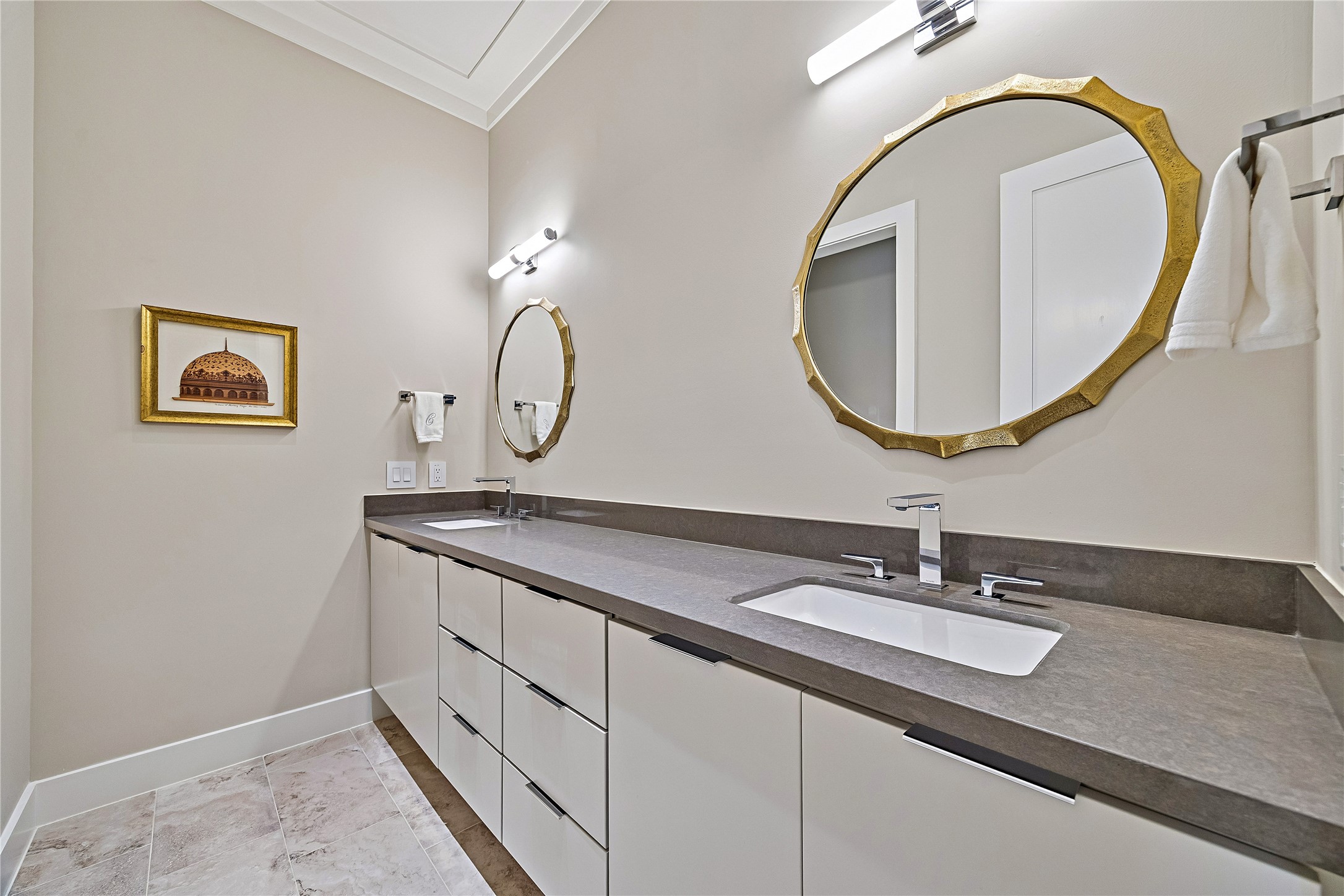 Beautifully appointed bathroom featuring a wide vanity with dual sinks, elegant countertop, decorative mirrors, and refined lighting. Thoughtfully coordinated finishes complement the home's sophisticated interior design.