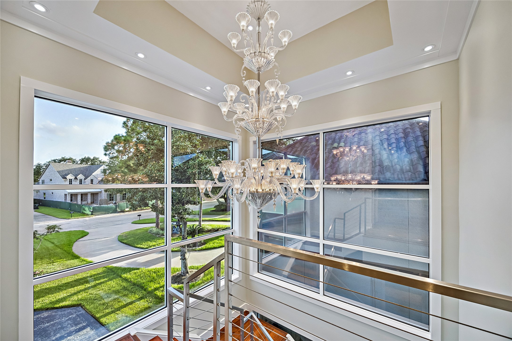 A dramatic architectural perspective showcasing an ornate chandelier suspended beside expansive windows overlooking the lush golf-course landscape. Natural light and elevated views emphasize the connection between the residence and its surroundings.