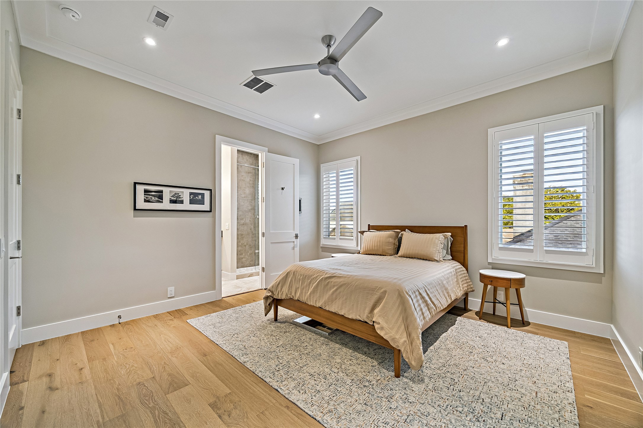 Bright upper-level bedroom featuring warm wood flooring, recessed lighting, a ceiling fan, and large windows. An inviting space with flexibility for bedroom furnishings and personal storage.