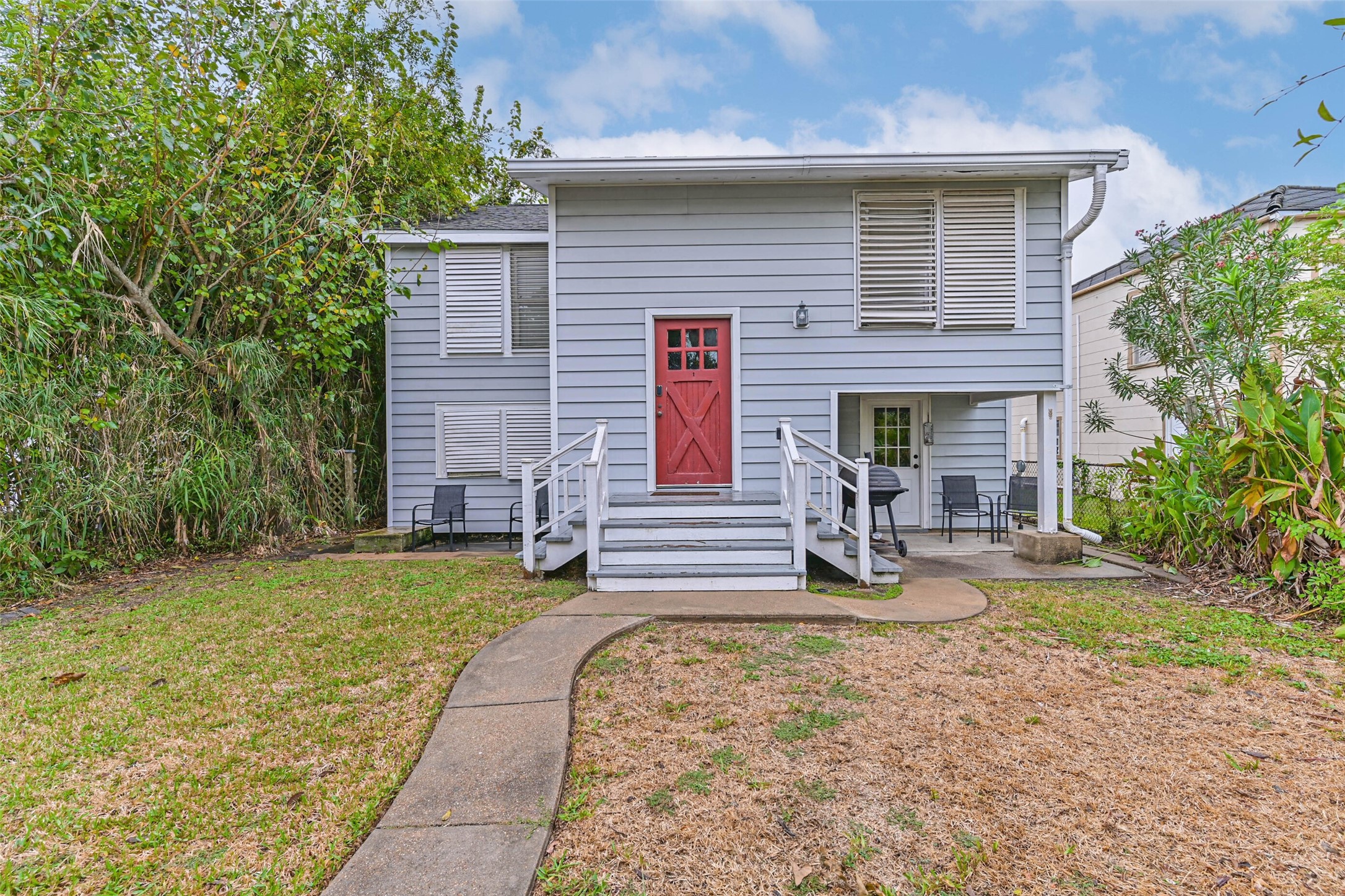 A charming entrance welcomes you home with a distinctive red front door, inviting entry stairs, and a peaceful outdoor setting.