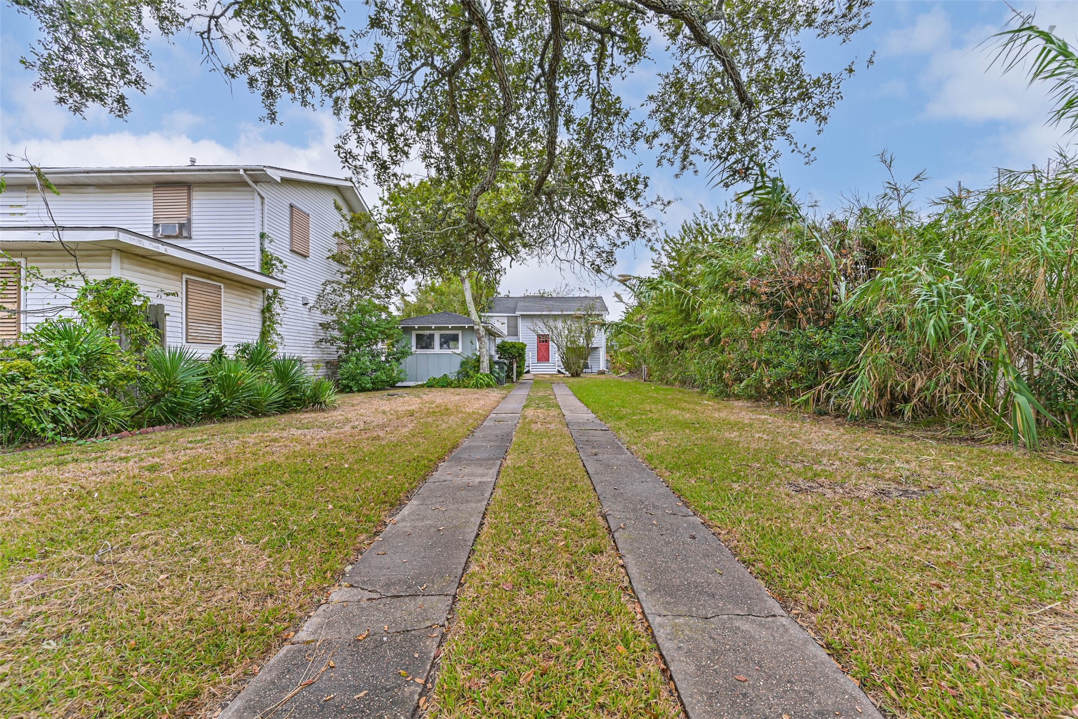 A welcoming view of the property with a paved walkway leading toward the home, surrounded by greenery and mature trees.