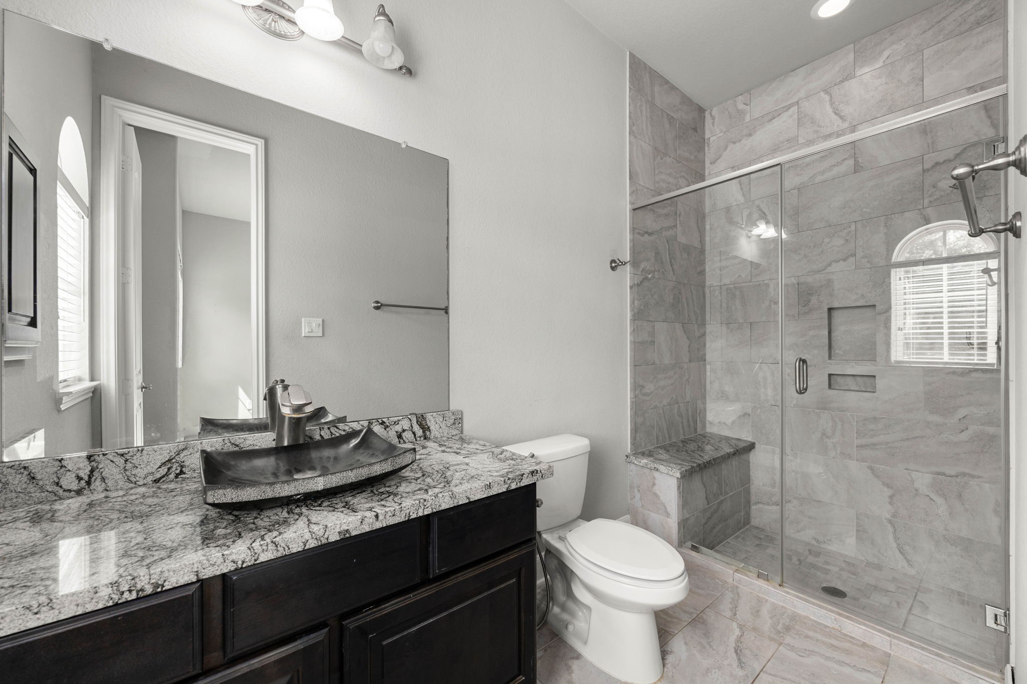 A private ensuite serves the downstairs secondary bedroom, featuring a vessel sink, striking counters, and a walk-in glass shower with a built-in bench.