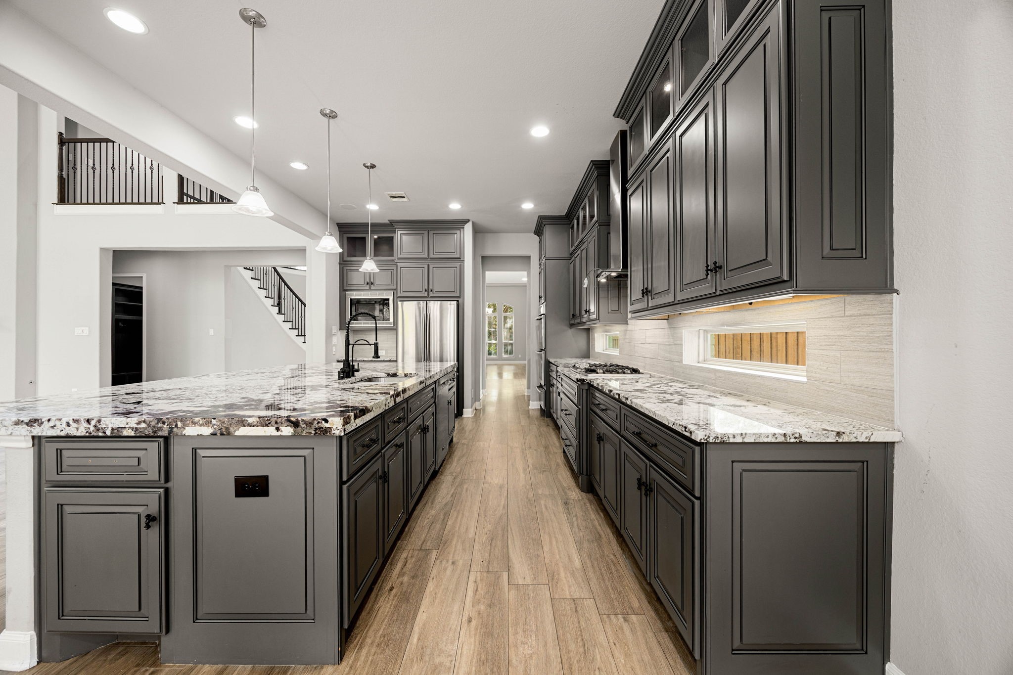 A long galley-style layout maximizes counter space in this kitchen, where Marble countertops, dark cabinetry, and a view straight through to the staircase and living area create a well-connected floor plan.