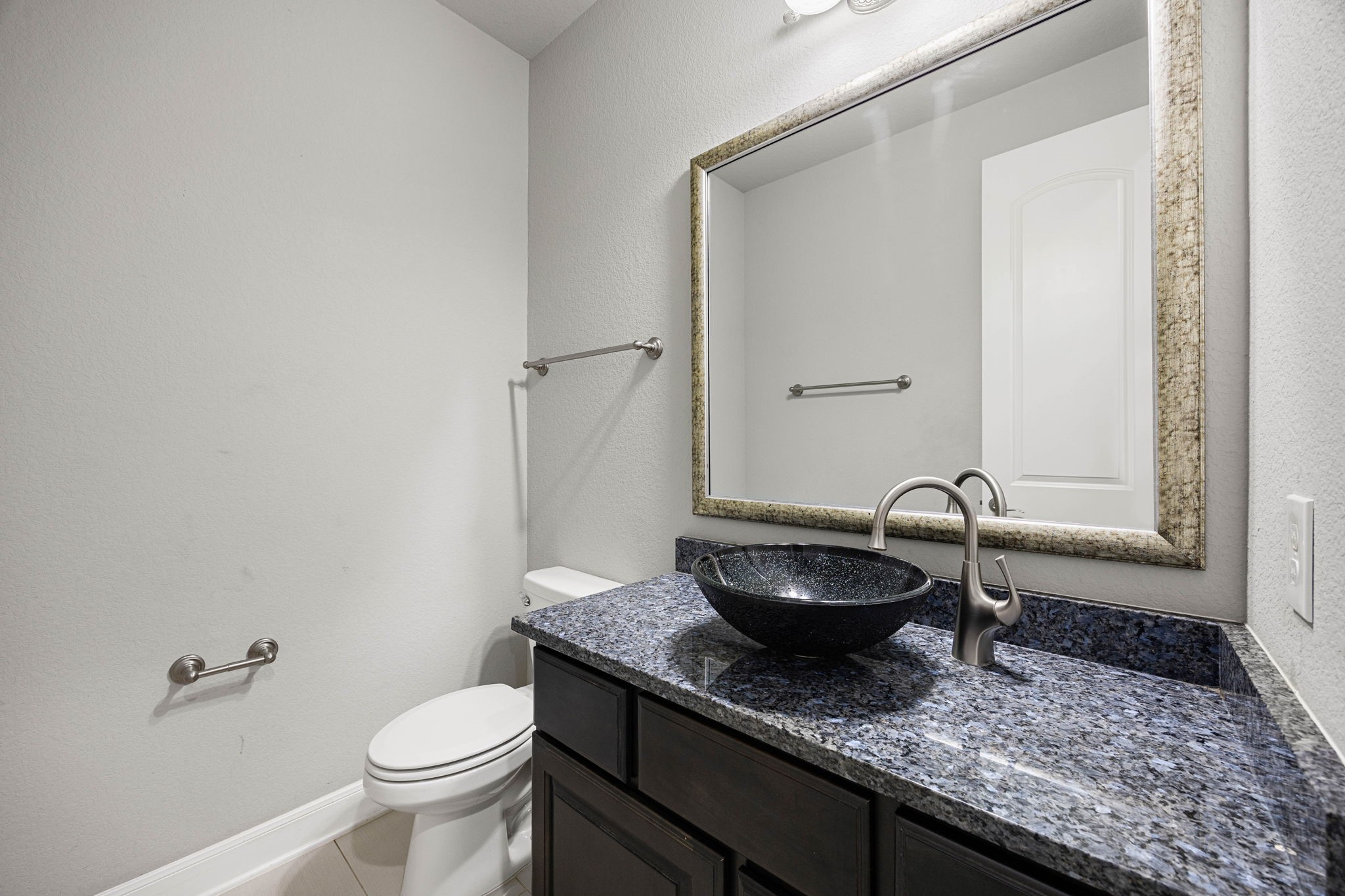 A striking vessel sink in speckled glass tops the granite vanity in this secondary bath, paired with a sleek gooseneck faucet for a modern, upgraded touch.