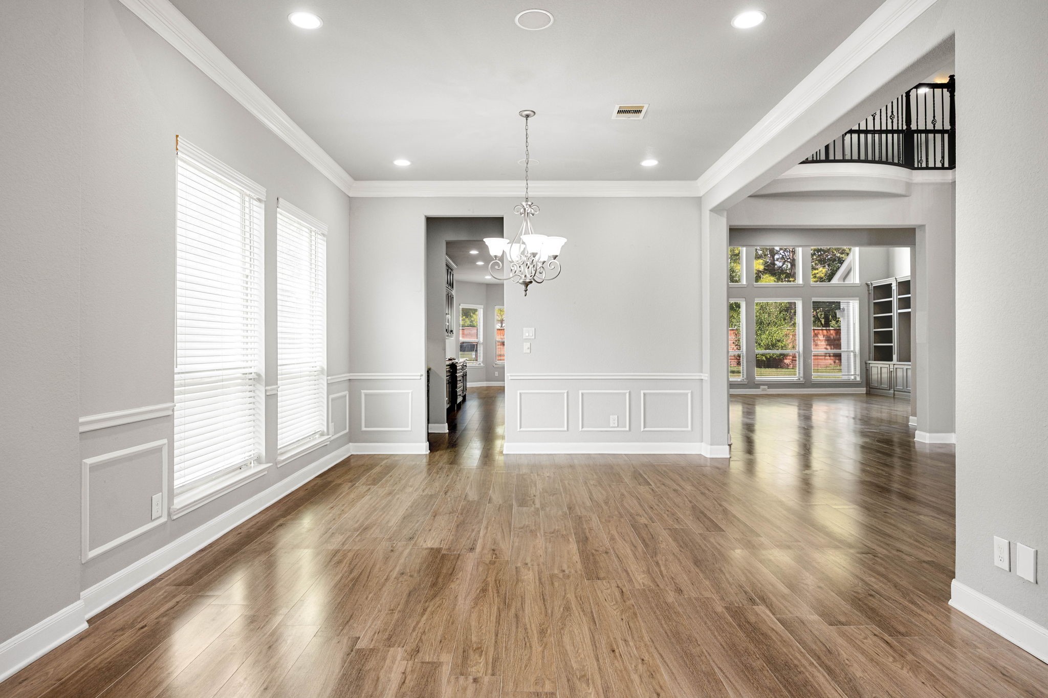 Wainscoting and a chandelier lend a polished, formal touch to the dining area, which flows openly toward the kitchen and two-story living space beyond.