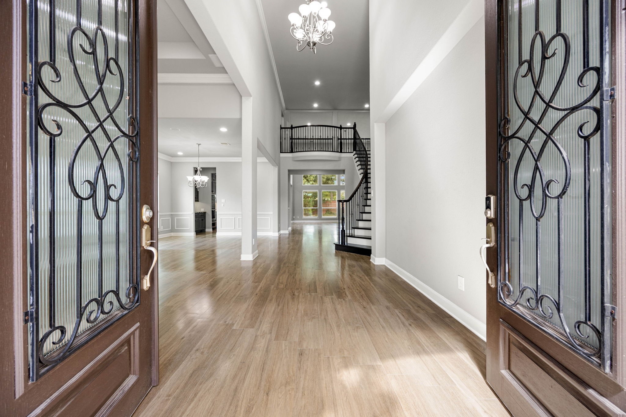 A dramatic two-story foyer welcomes you in, where a wrought-iron staircase and railing wind gracefully beneath a crystal chandelier, opening directly into the home's light-filled main living spaces.