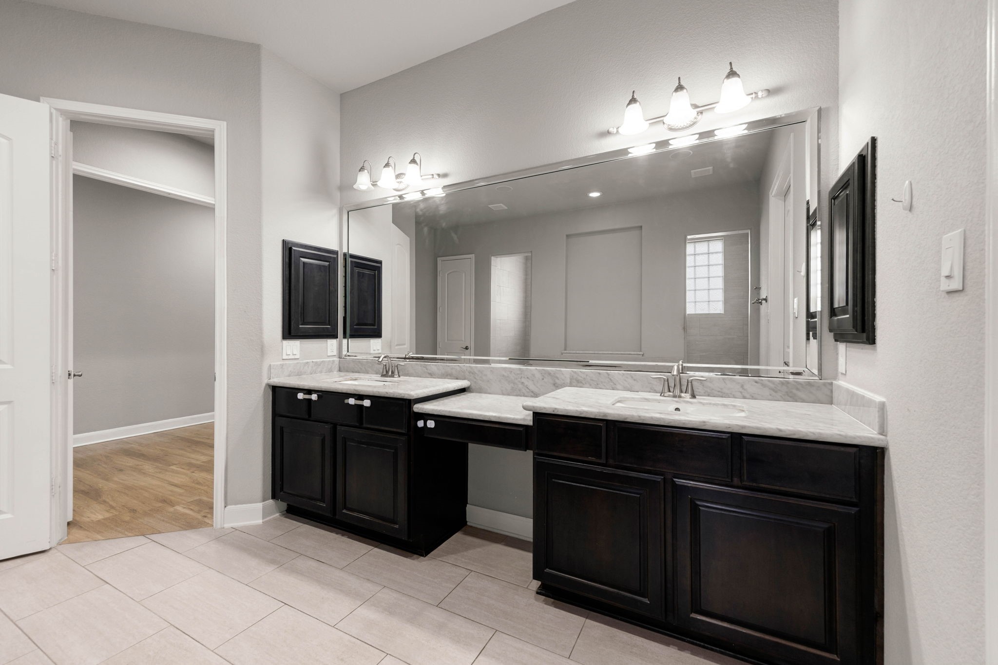 This primary ensuite features a dual-sink vanity with marble counters, a private makeup vanity space, and dark wood cabinetry for a polished, modern look.