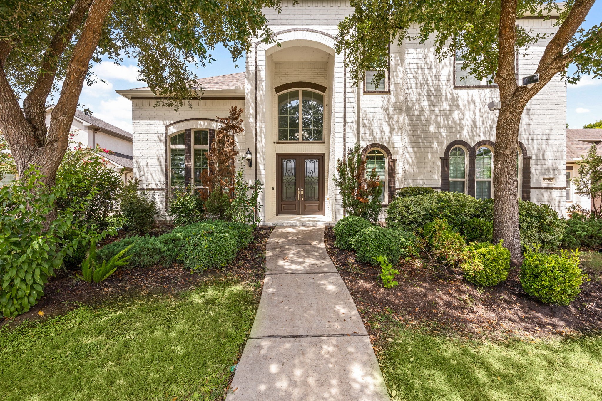 A closer look at the front entrance highlights the homes distinctive arched architecture, stately double doors, and mature landscaping that frames the approach.