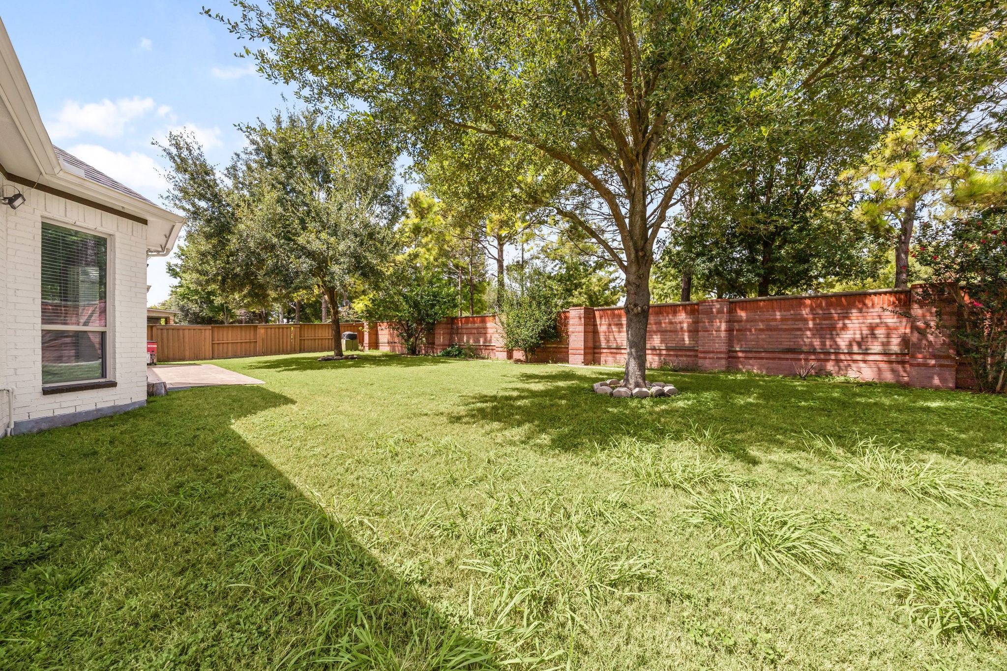 Another angle of the fenced backyard highlights its generous size and mature landscaping, with a covered patio just off the home's rear entrance.