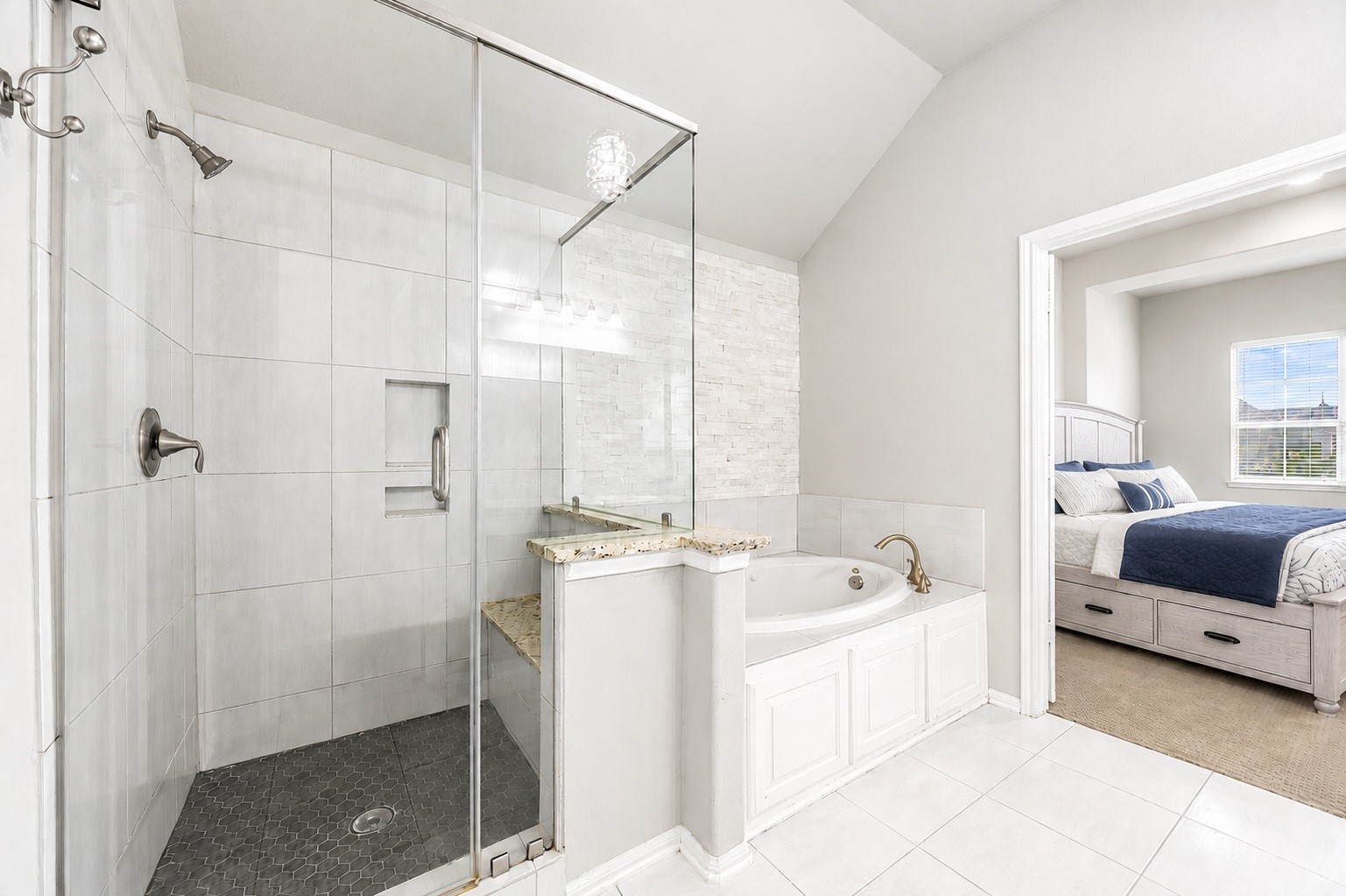 This ensuite pairs a walk-in glass shower with a jetted soaking tub set beneath a stacked-stone accent wall, offering direct access to the second primary suite.