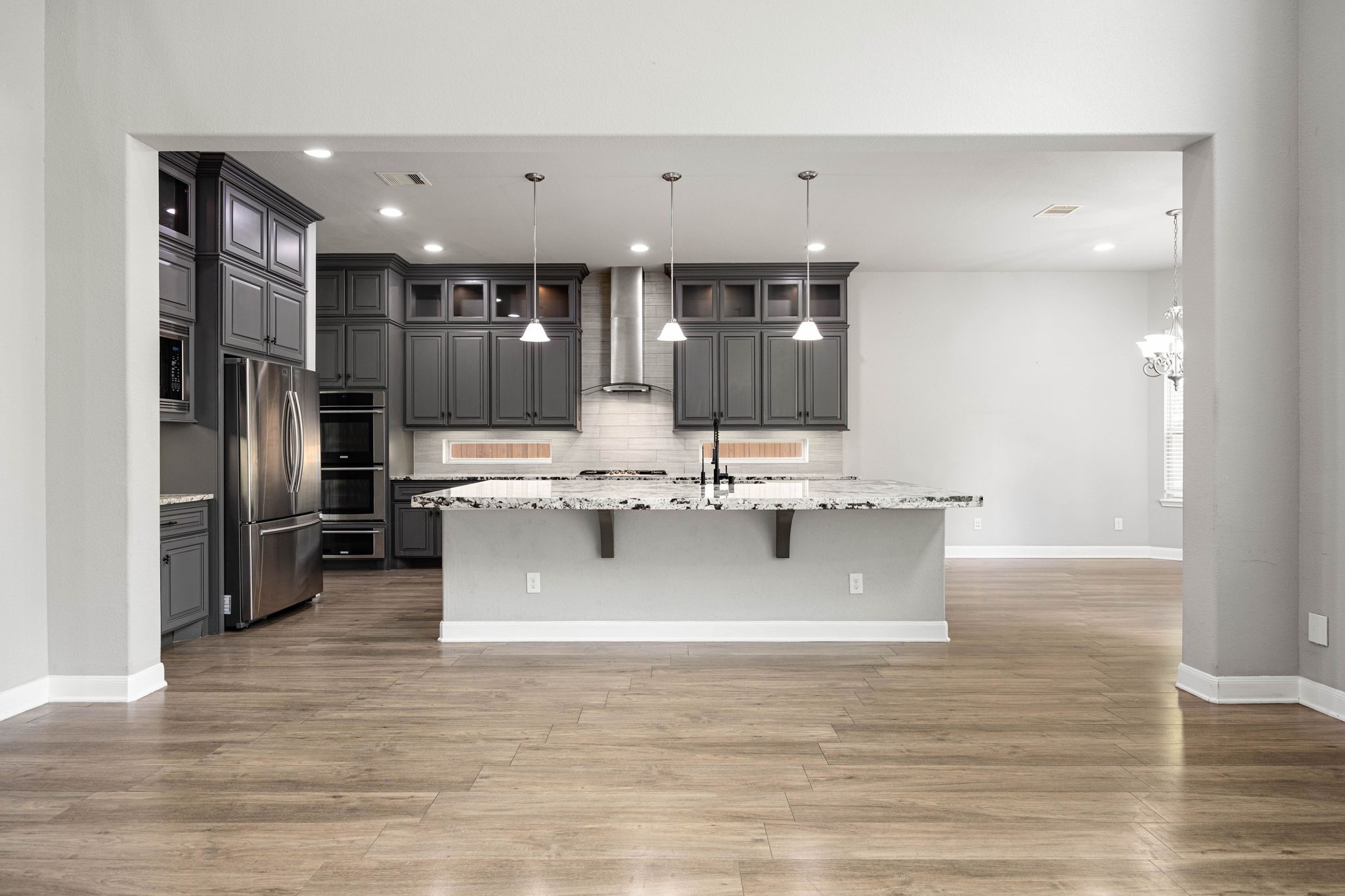 Rich dark cabinetry and a stainless steel hood vent frame this open-concept kitchen, where a large center island with pendant lighting and granite counters flows seamlessly into the main living space.
