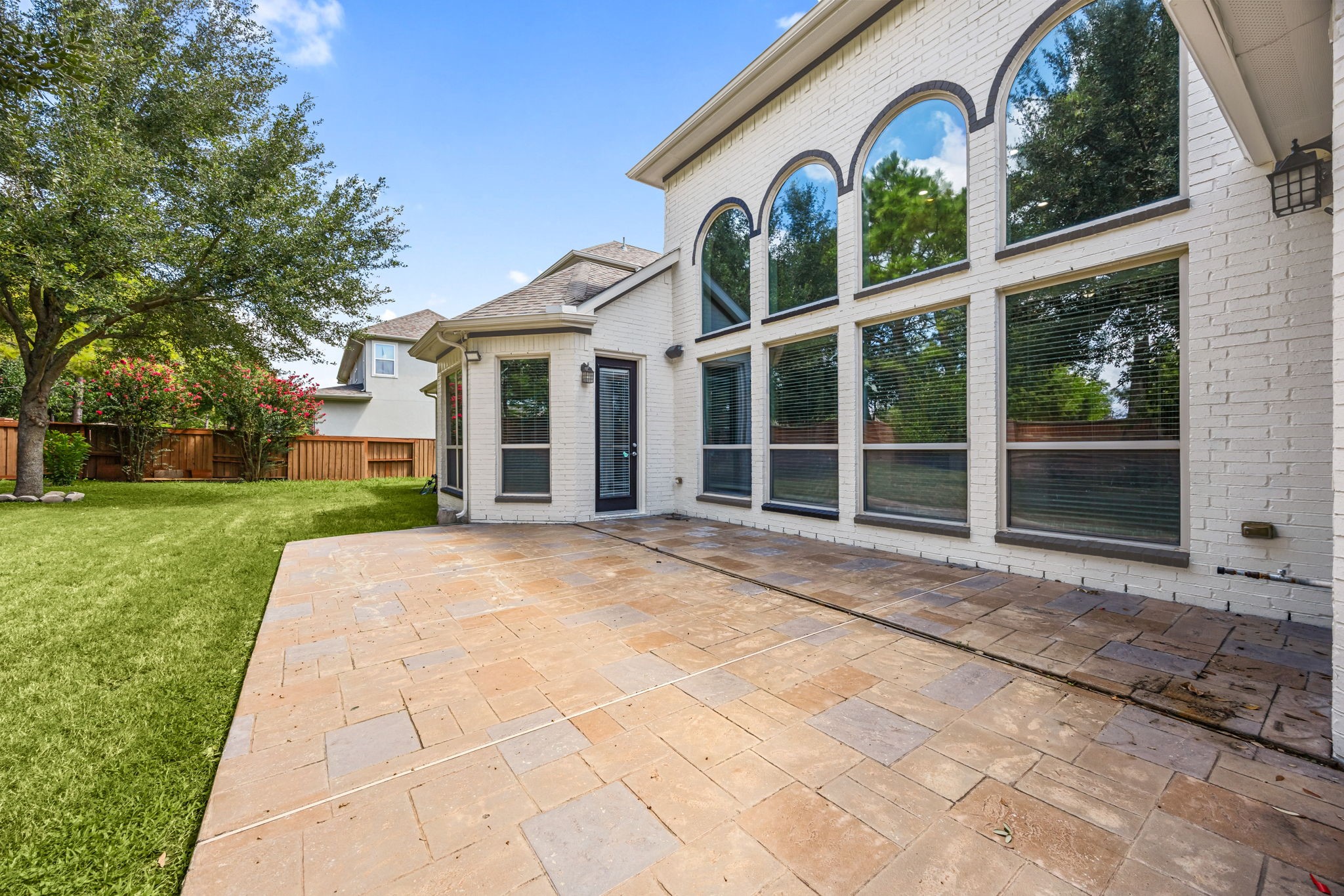 The stamped-concrete patio extends along the back of the home, framed by the dramatic two-story arched windows above  a versatile space for outdoor dining or relaxing.