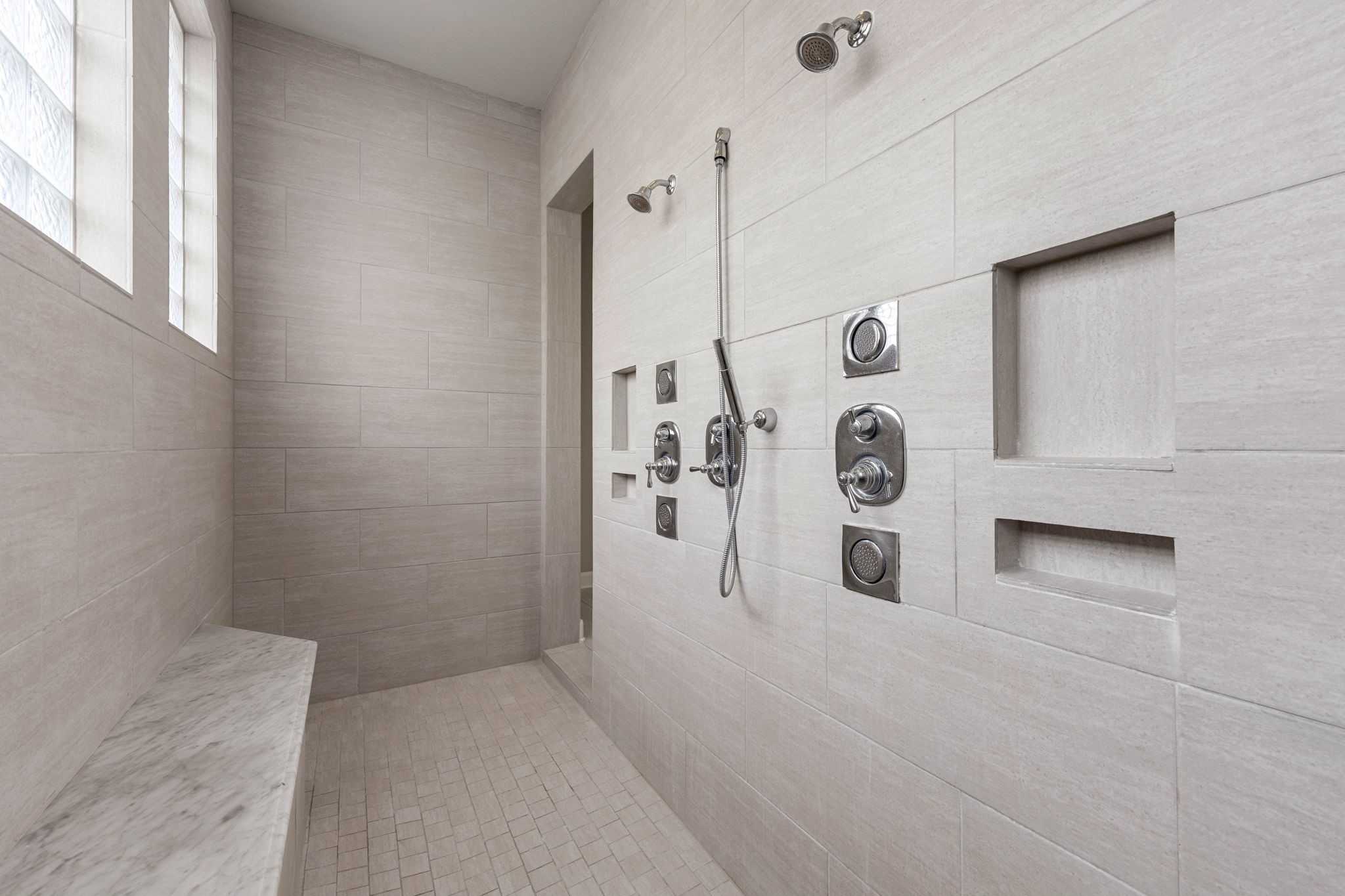The oversized walk-in shower features dual shower heads, a handheld sprayer, and built-in niches, offering a spacious, modern showering experience.