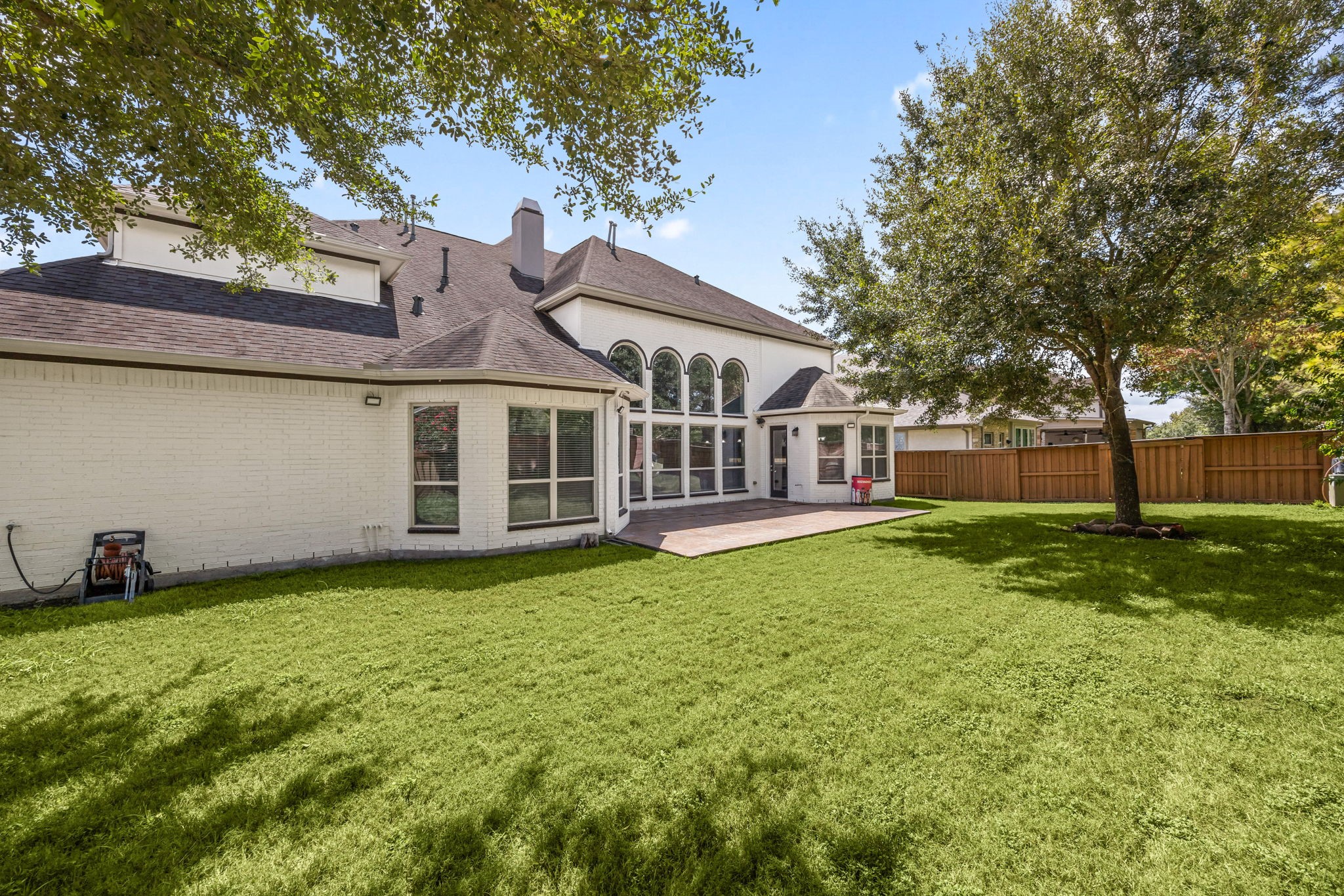 A spacious backyard offers plenty of room to enjoy, bordered by a brick privacy wall and mature trees that create natural shade throughout the yard.