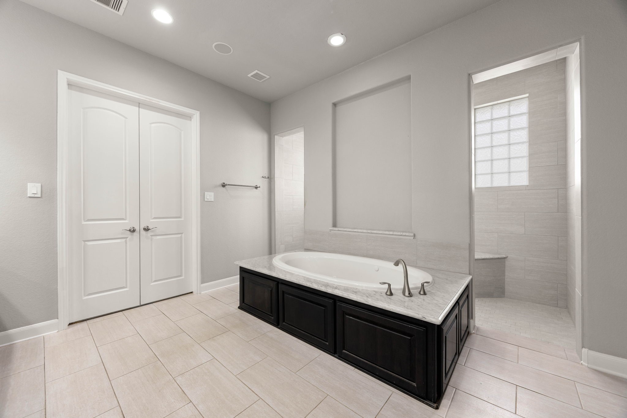 A jetted soaking tub takes center stage in this ensuite, framed by marble surround tile and positioned beside a separate walk-in shower for a true spa-like retreat.