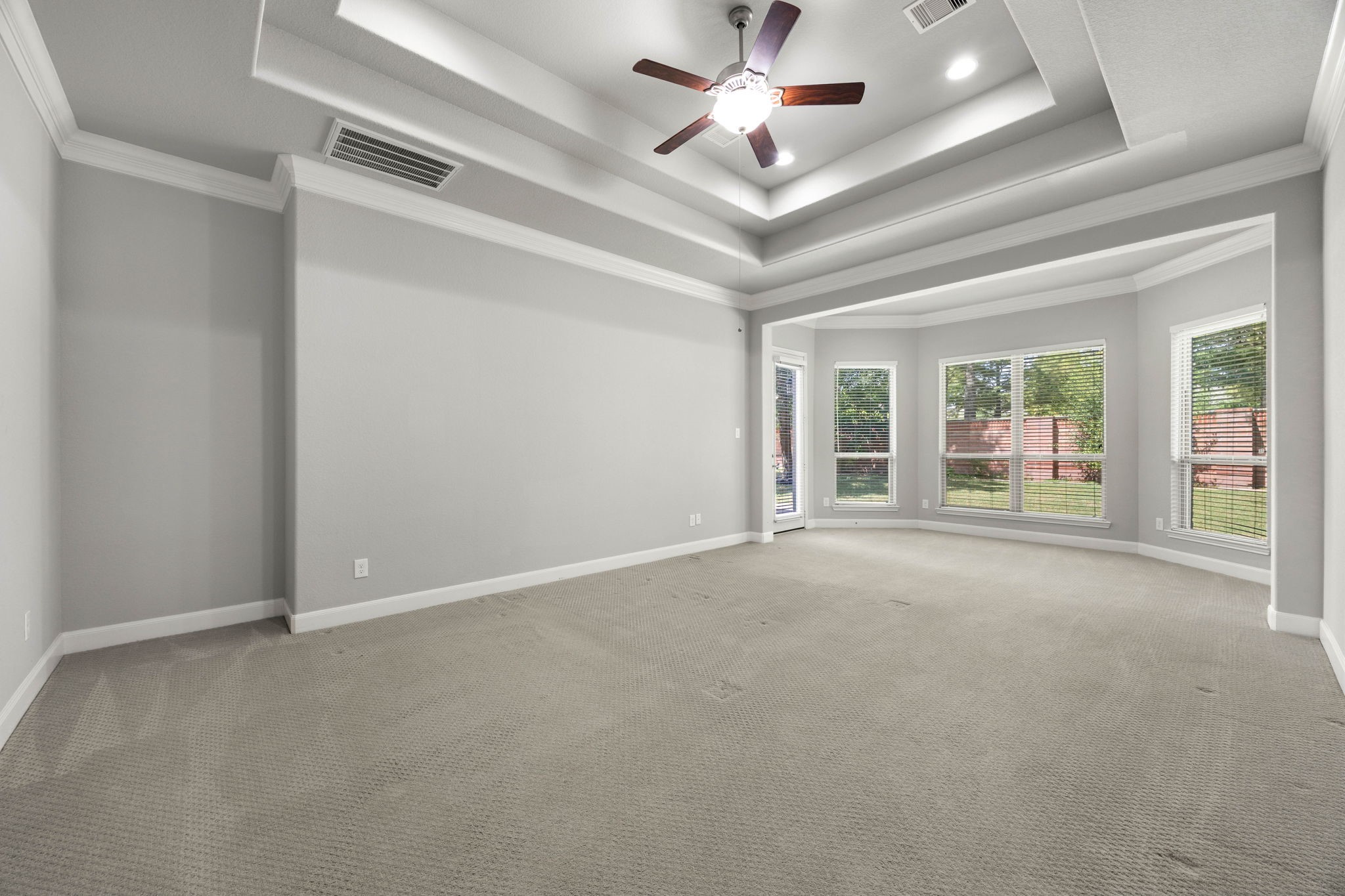 One of the home's two primary suites offers a generous tray ceiling and a bright bay-window sitting area, creating a versatile retreat with room to spare.