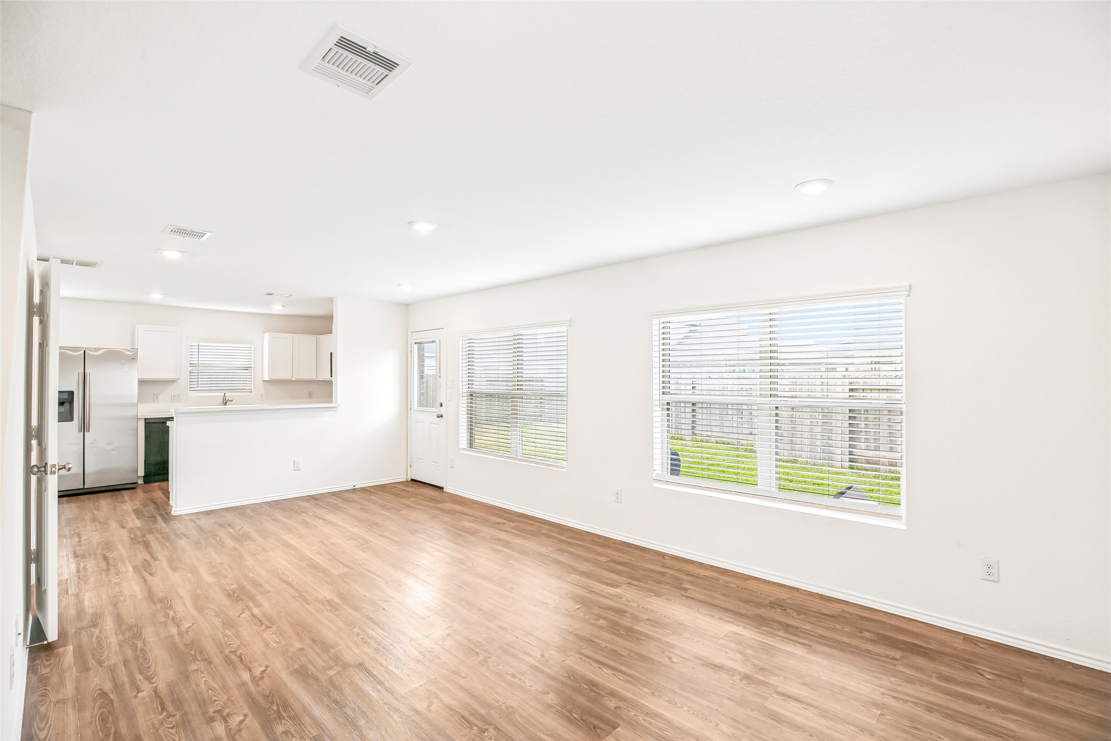 Bright open living and dining area with wood-look flooring, wide windows, and a connected kitchen view.