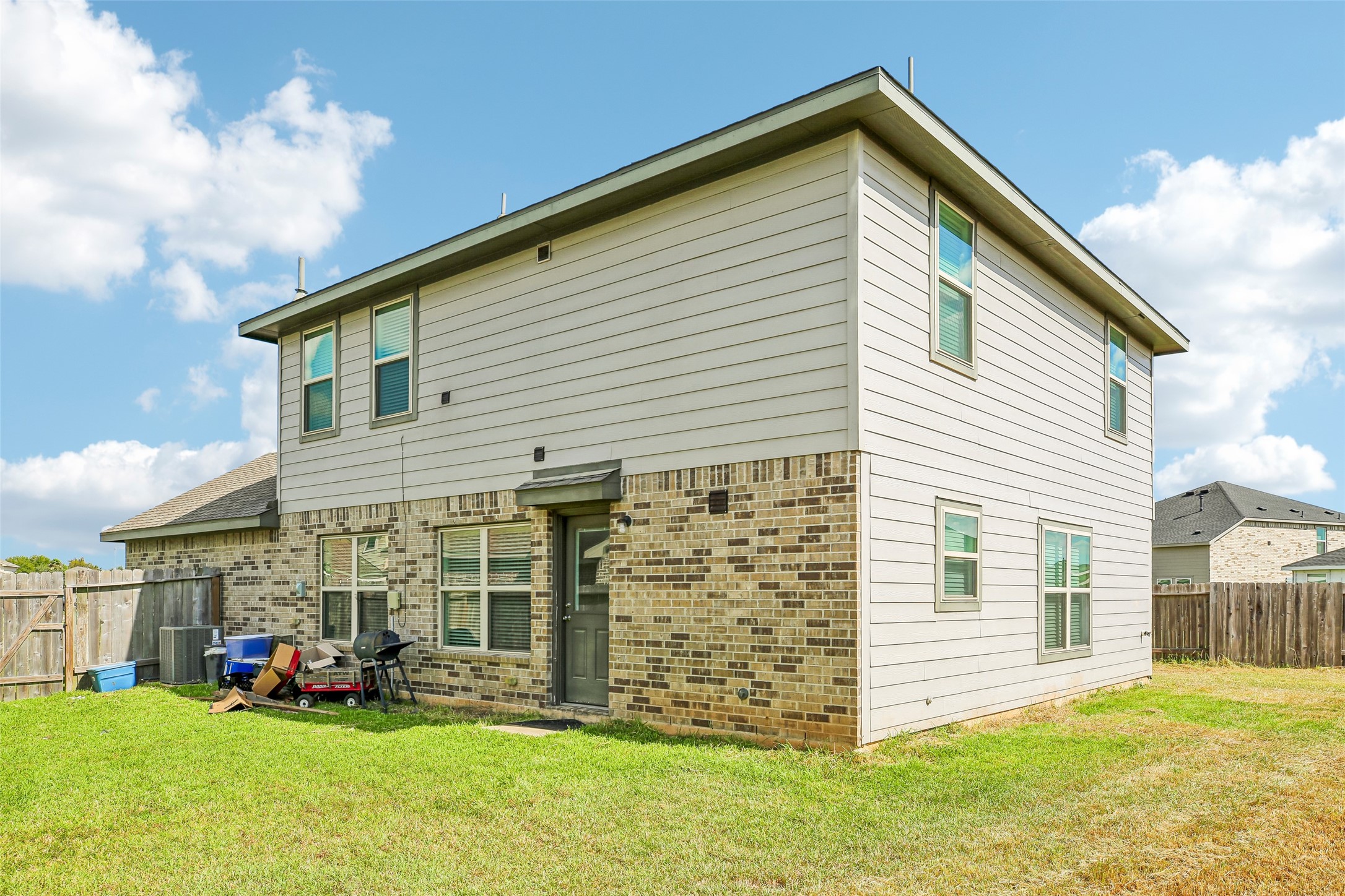 Rear exterior view showing the two-story brick-and-siding home, windows, rear door, fenced yard, and lawn.