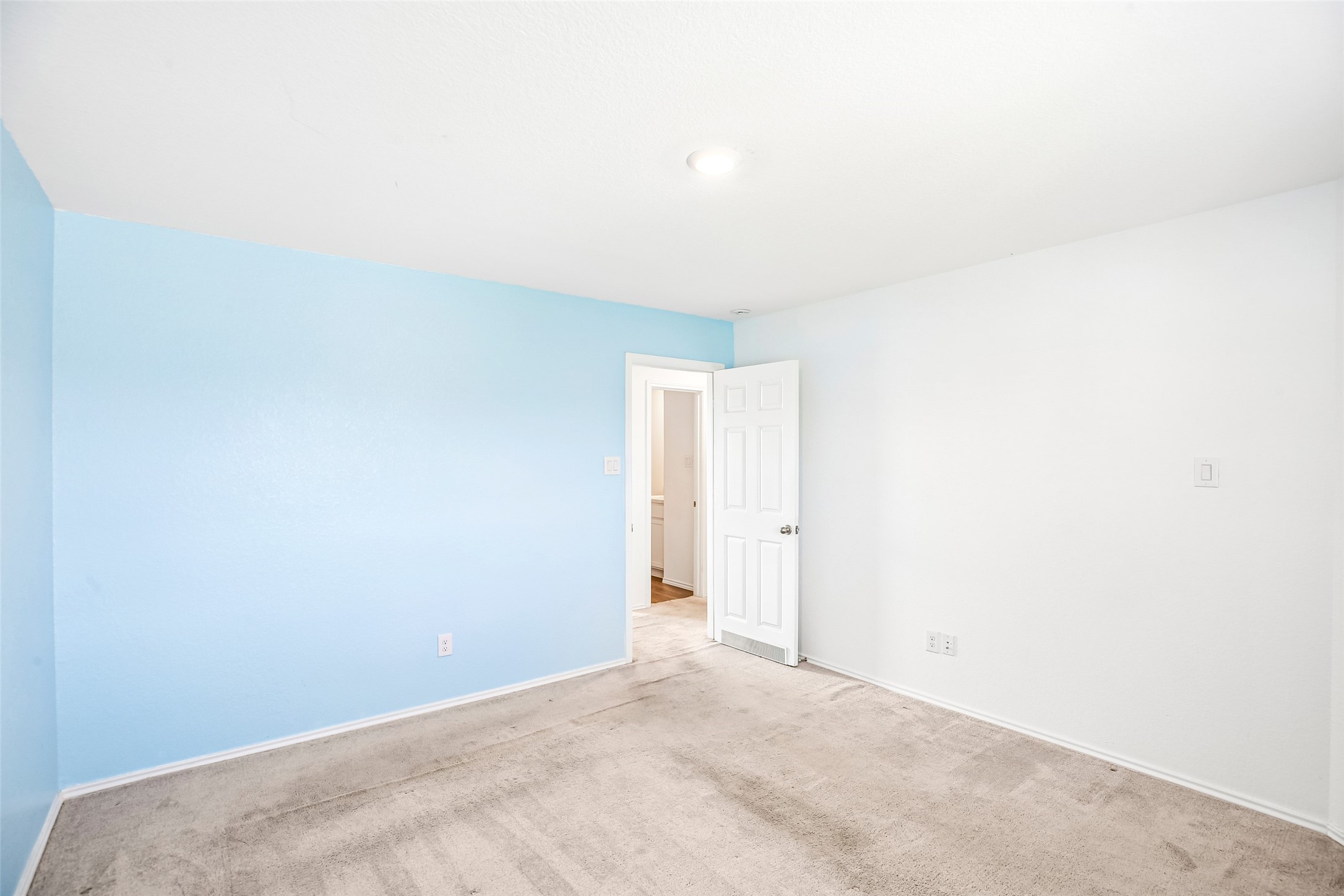 Empty carpeted room with a blue accent wall and open doorway.