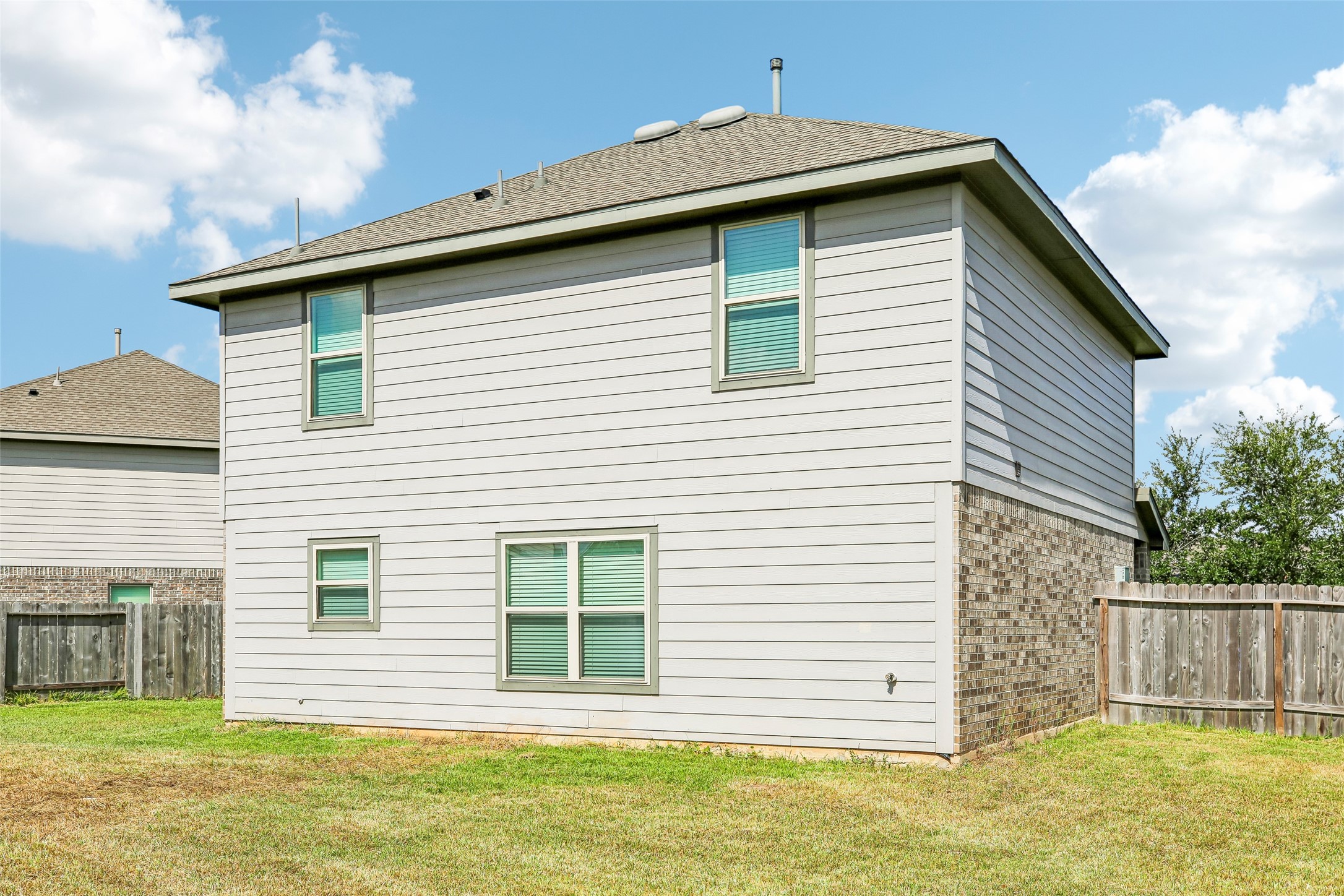 Rear exterior view of the home from the fenced side yard, showing siding, brick, windows, roofline, and lawn.
