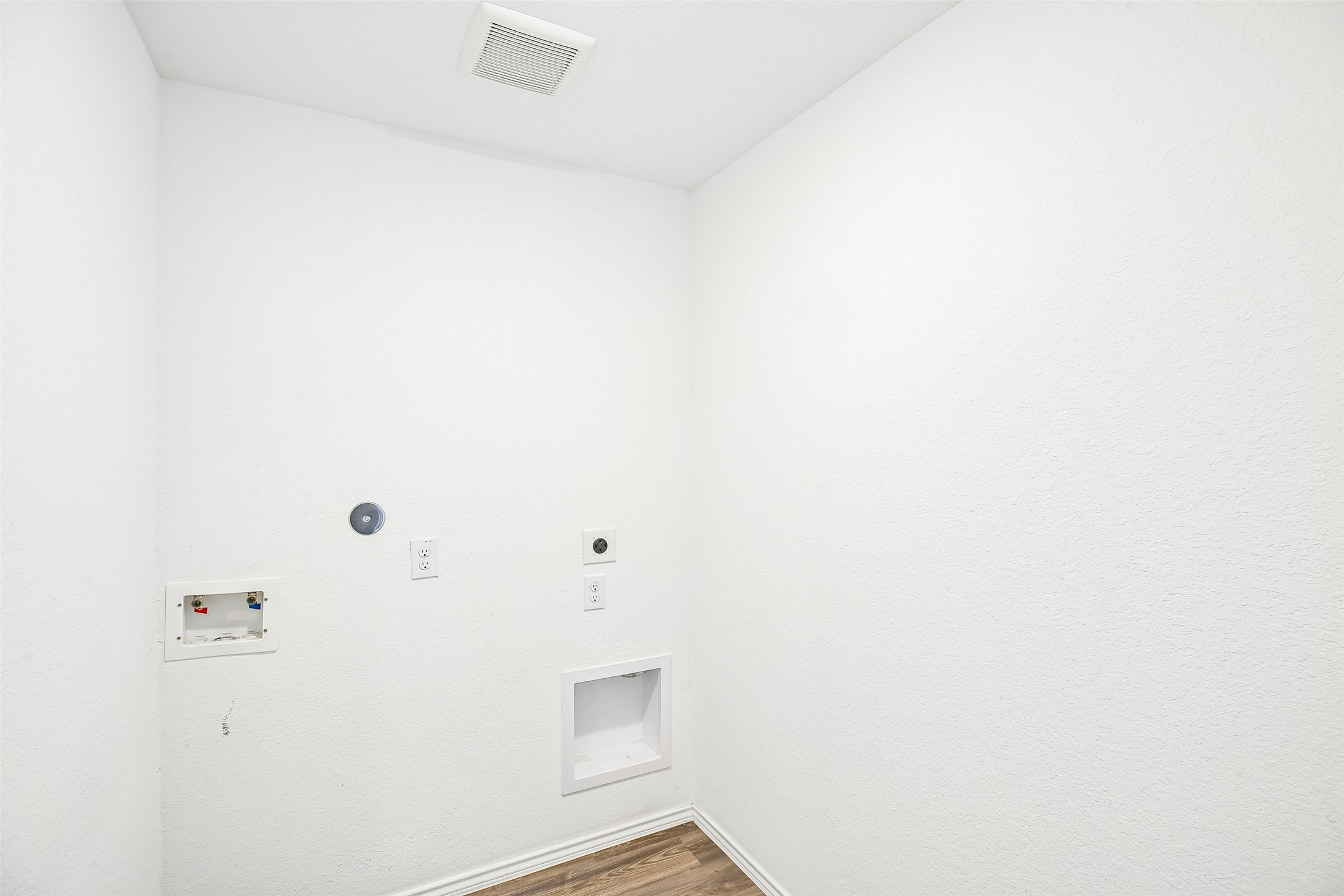 Empty interior utility-area corner with textured white walls, wall outlets and service boxes, a ceiling vent, and wood-look flooring.