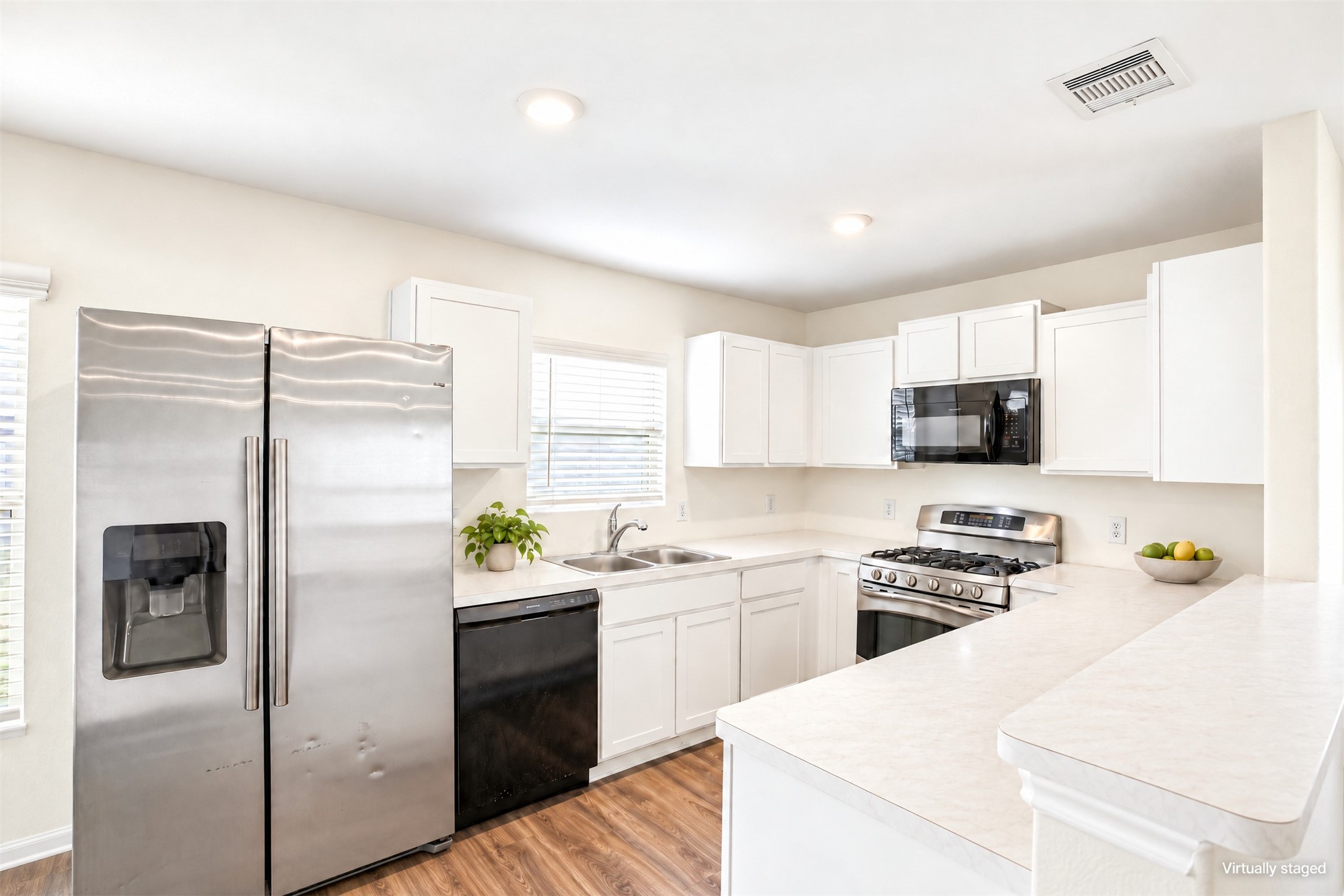 Bright kitchen with white cabinetry, light counters, stainless appliances, and wood-look flooring.