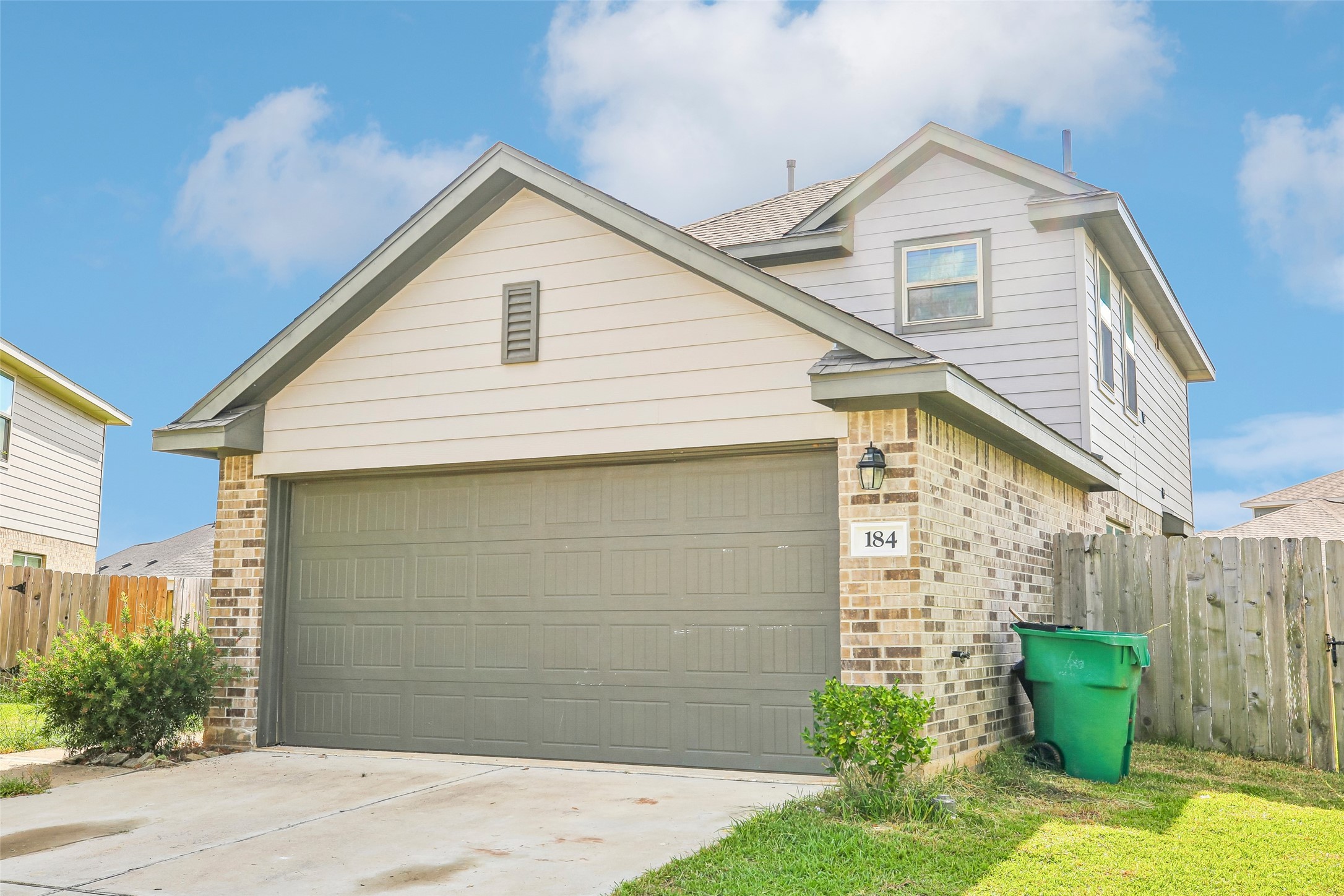 Front exterior view showing the attached garage, brick-and-siding facade, driveway, lawn, fencing, and landscaping.