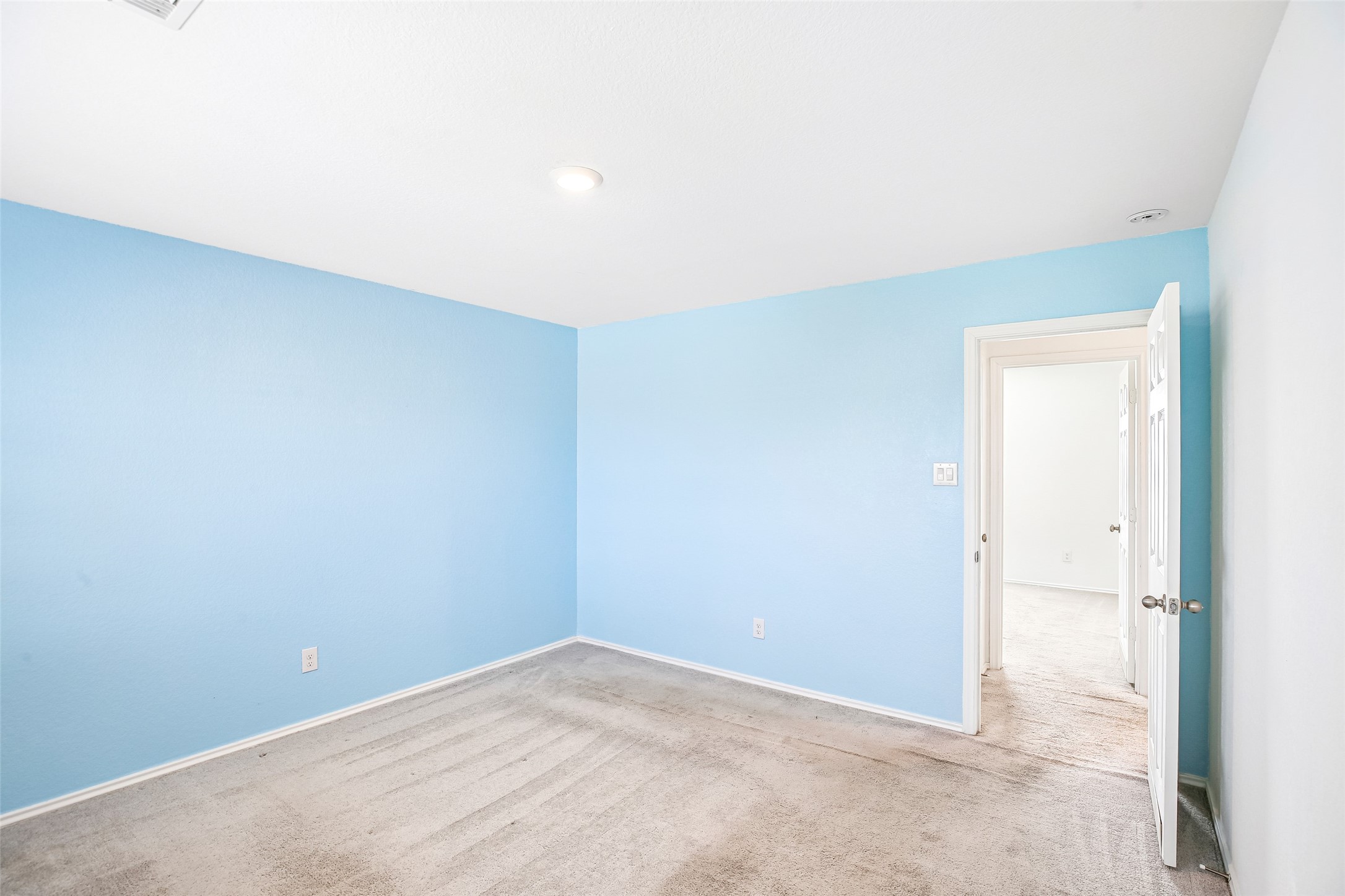 Empty carpeted room with blue-painted walls and an open doorway.