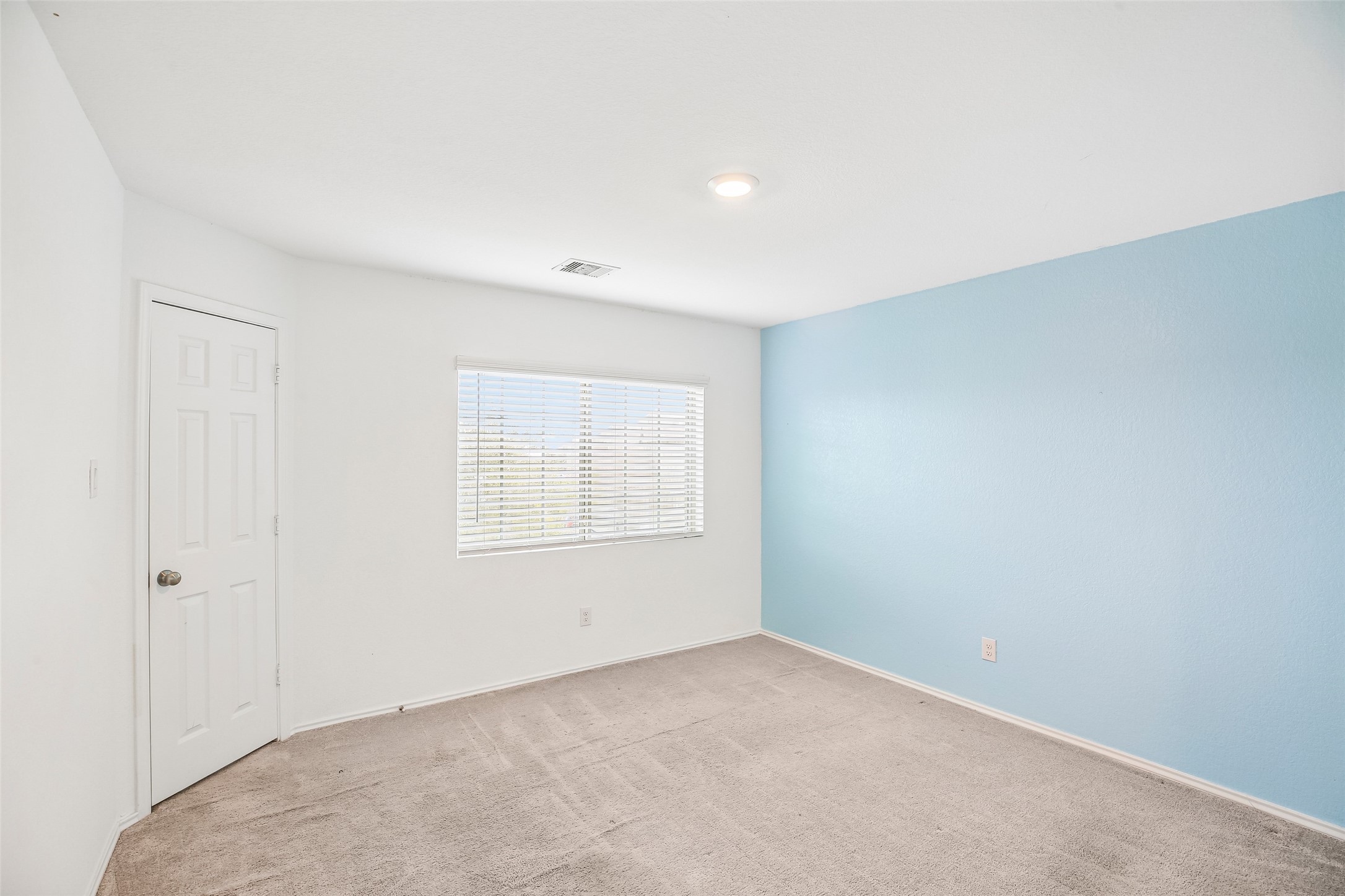 Empty carpeted interior room with a window, blinds, white door, and blue accent wall.