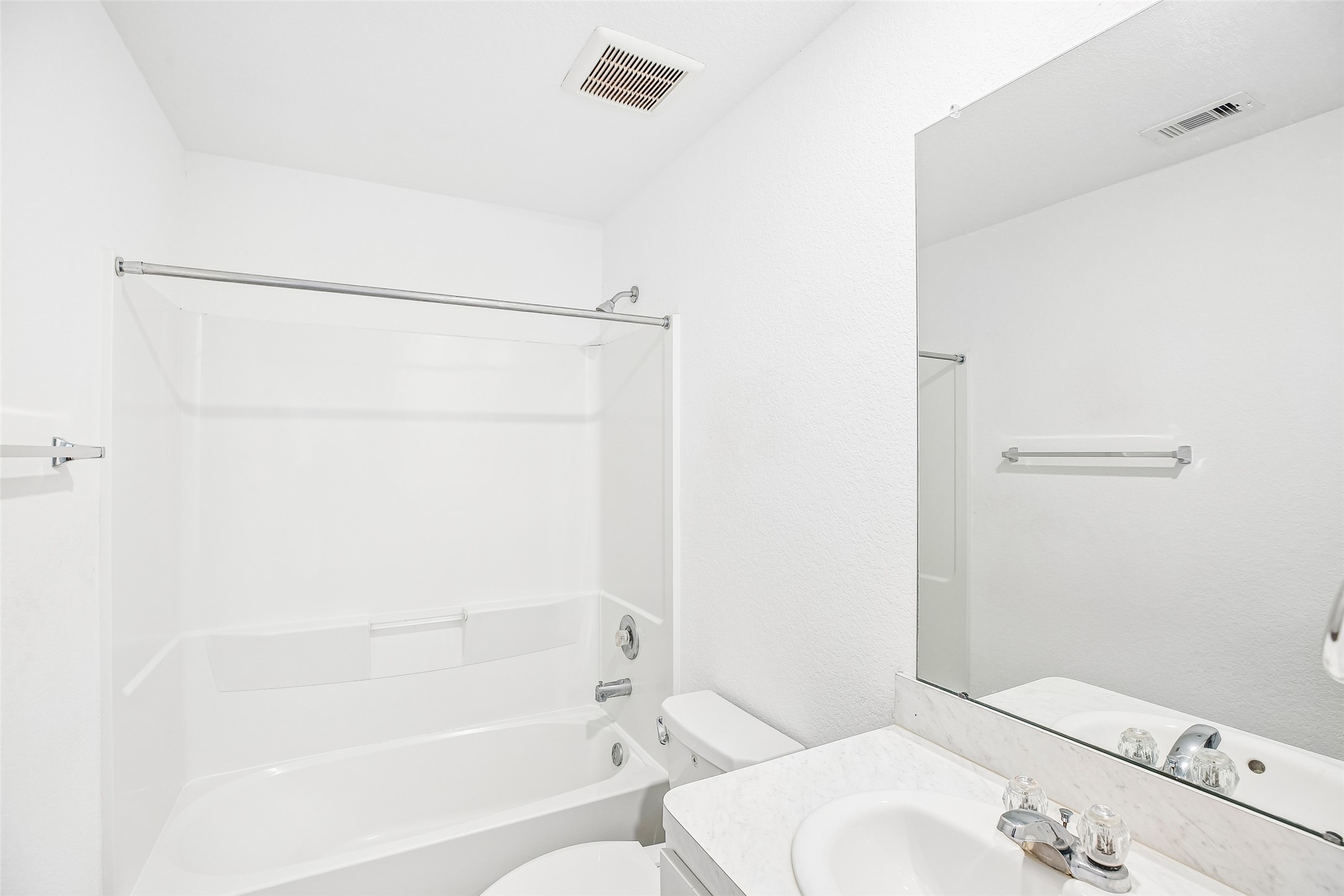 Bright bathroom with a tub/shower, vanity, mirrored wall, and neutral white finishes.