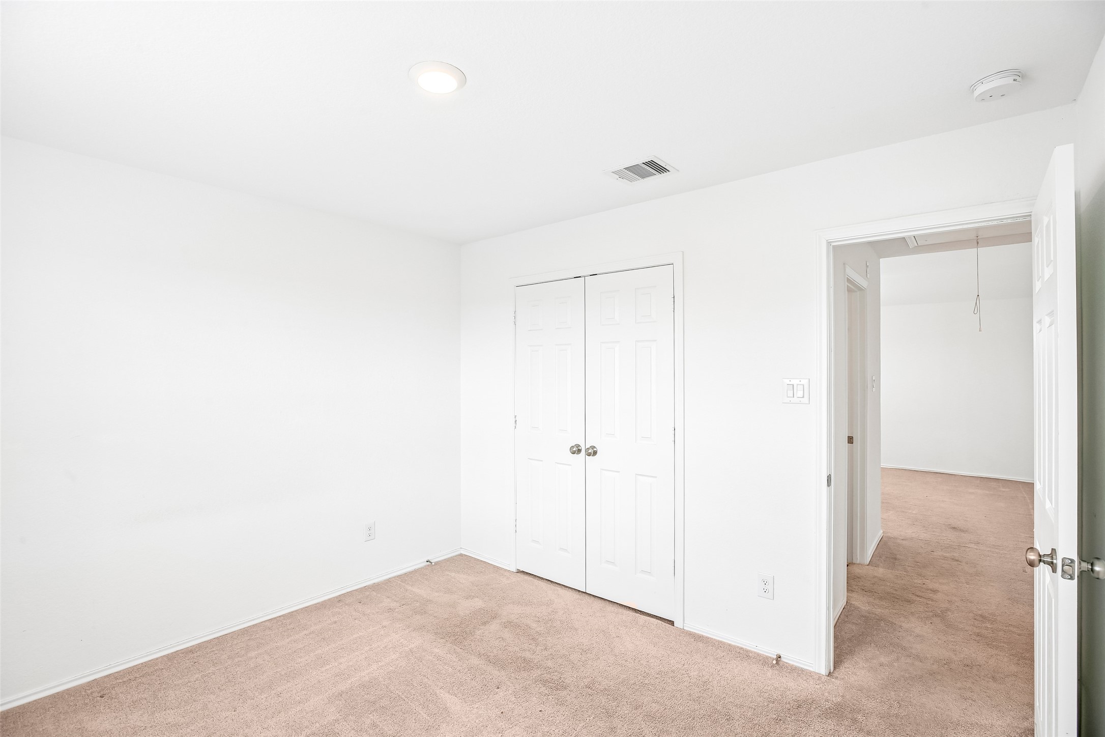 Empty carpeted room with double closet doors and an open doorway to the carpeted hall/adjacent room.