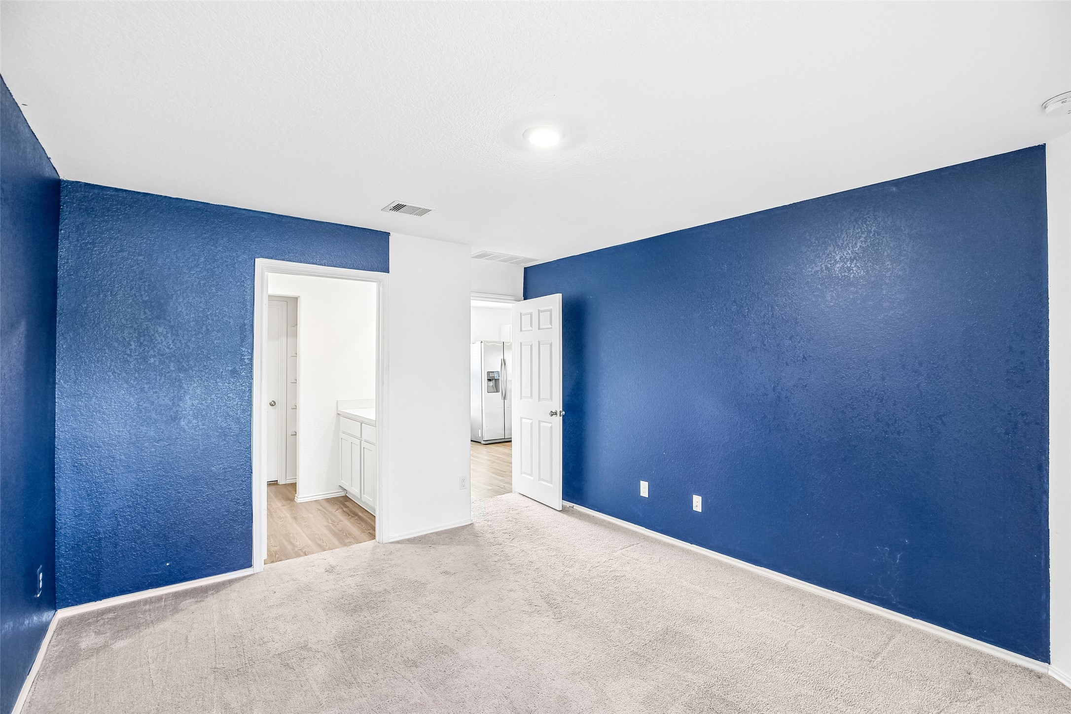 Empty carpeted room with blue accent walls, white trim and two open doorways to adjacent areas.