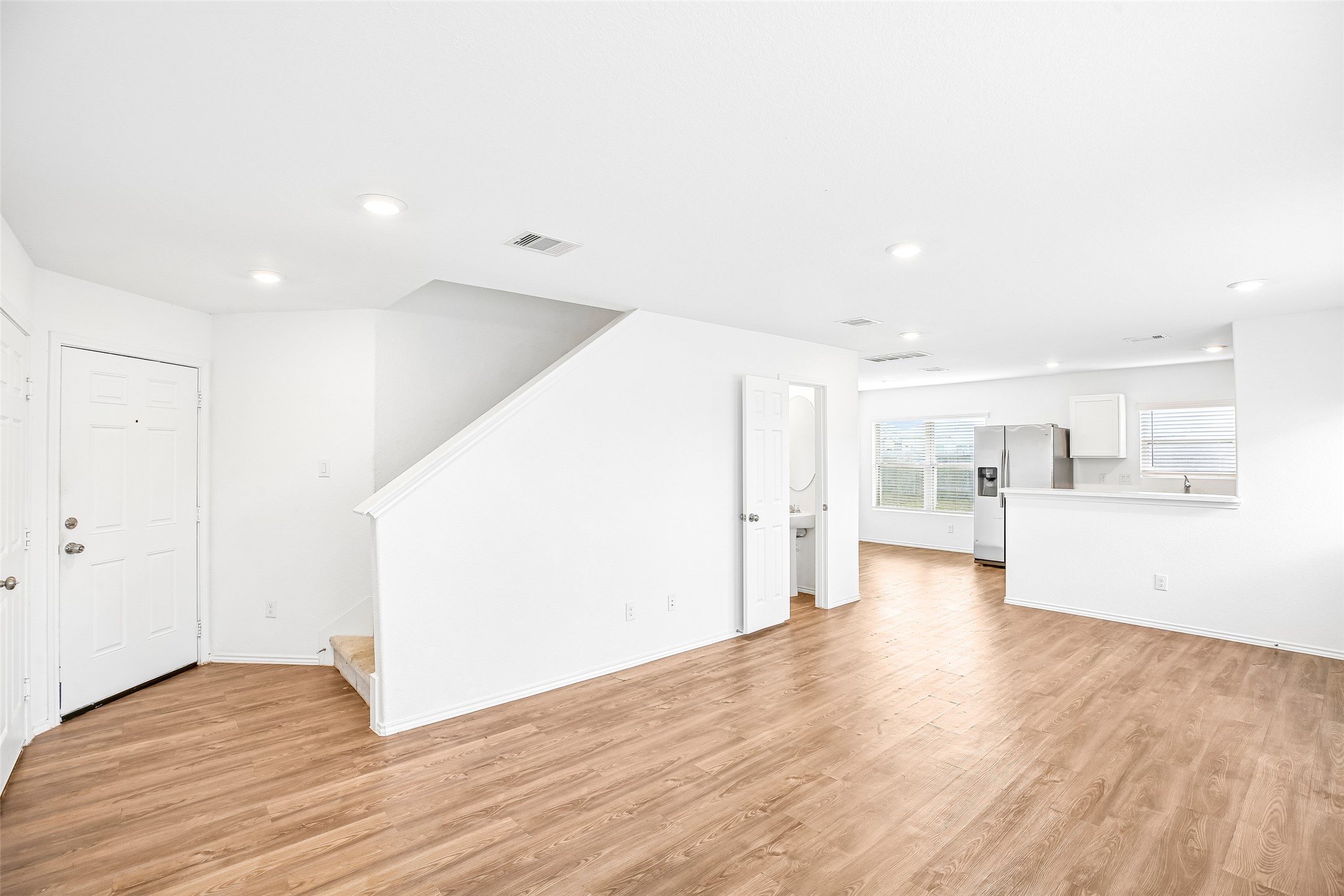 Open, empty living and dining area with wood-look flooring, stairs, and a connected kitchen view.