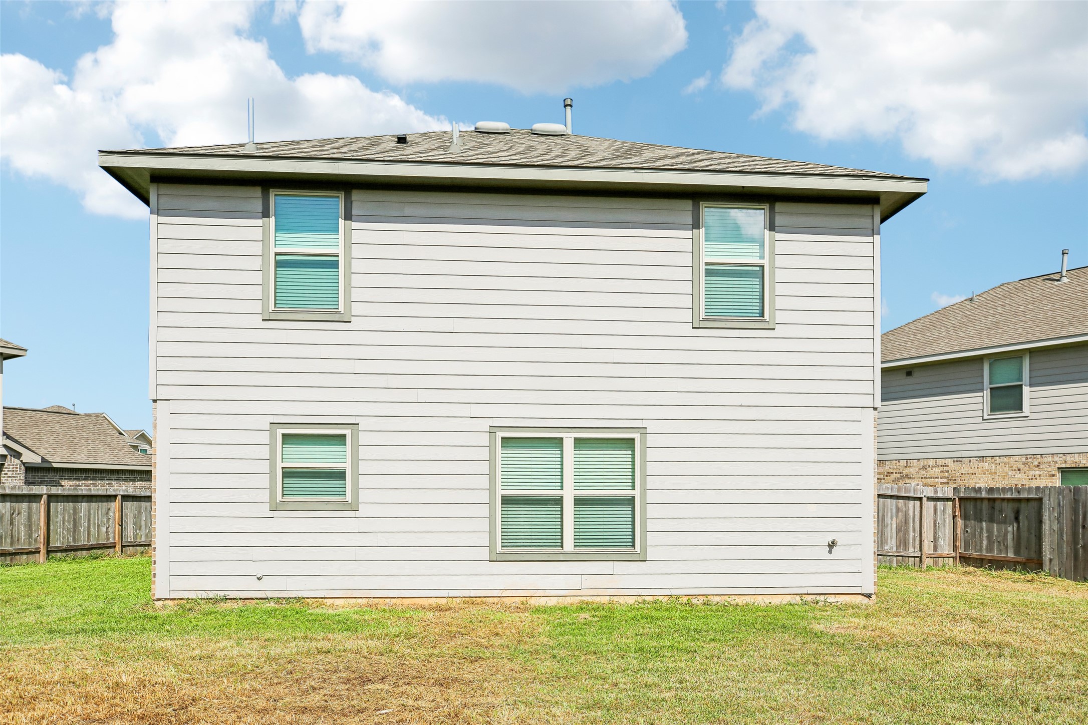 Rear exterior elevation viewed from the backyard, showing the home's siding, windows, fencing, and yard.