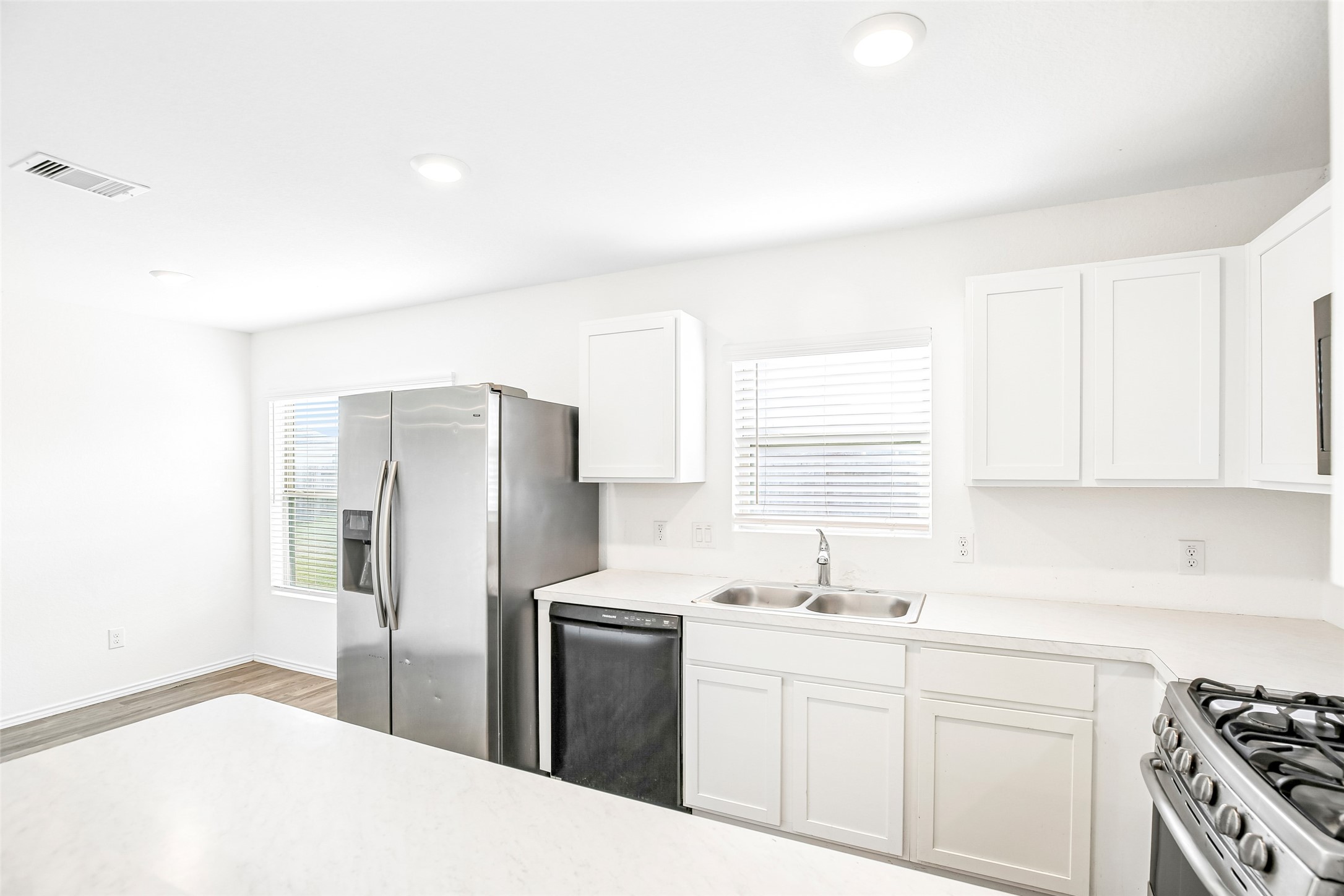 Kitchen view showing white cabinetry, stainless appliances, sink, counters, and the adjacent dining area.