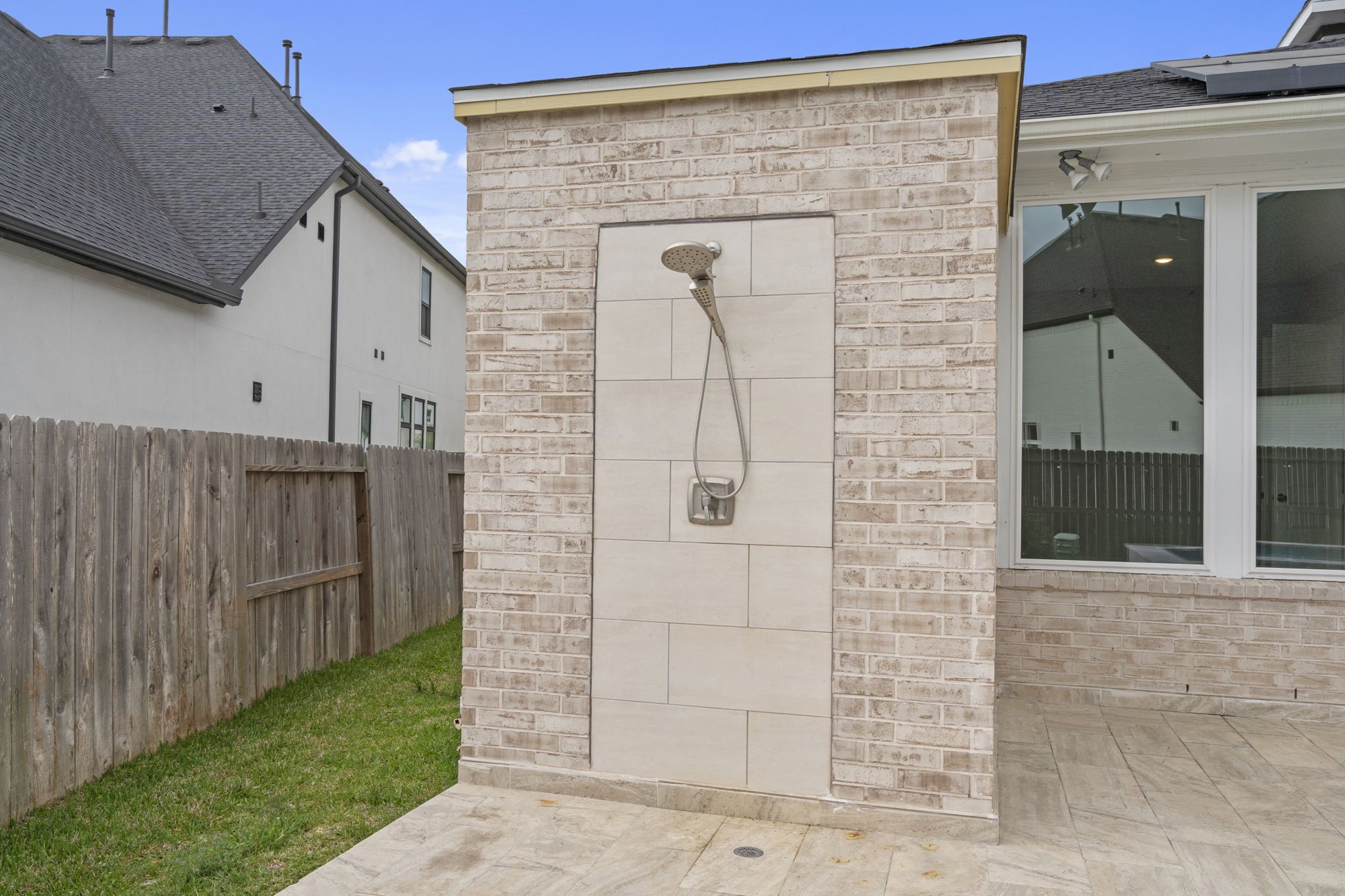 Outdoor shower area adding convenience to the pool experience. There is a full bath behind the shower area connecting outdoors as well.