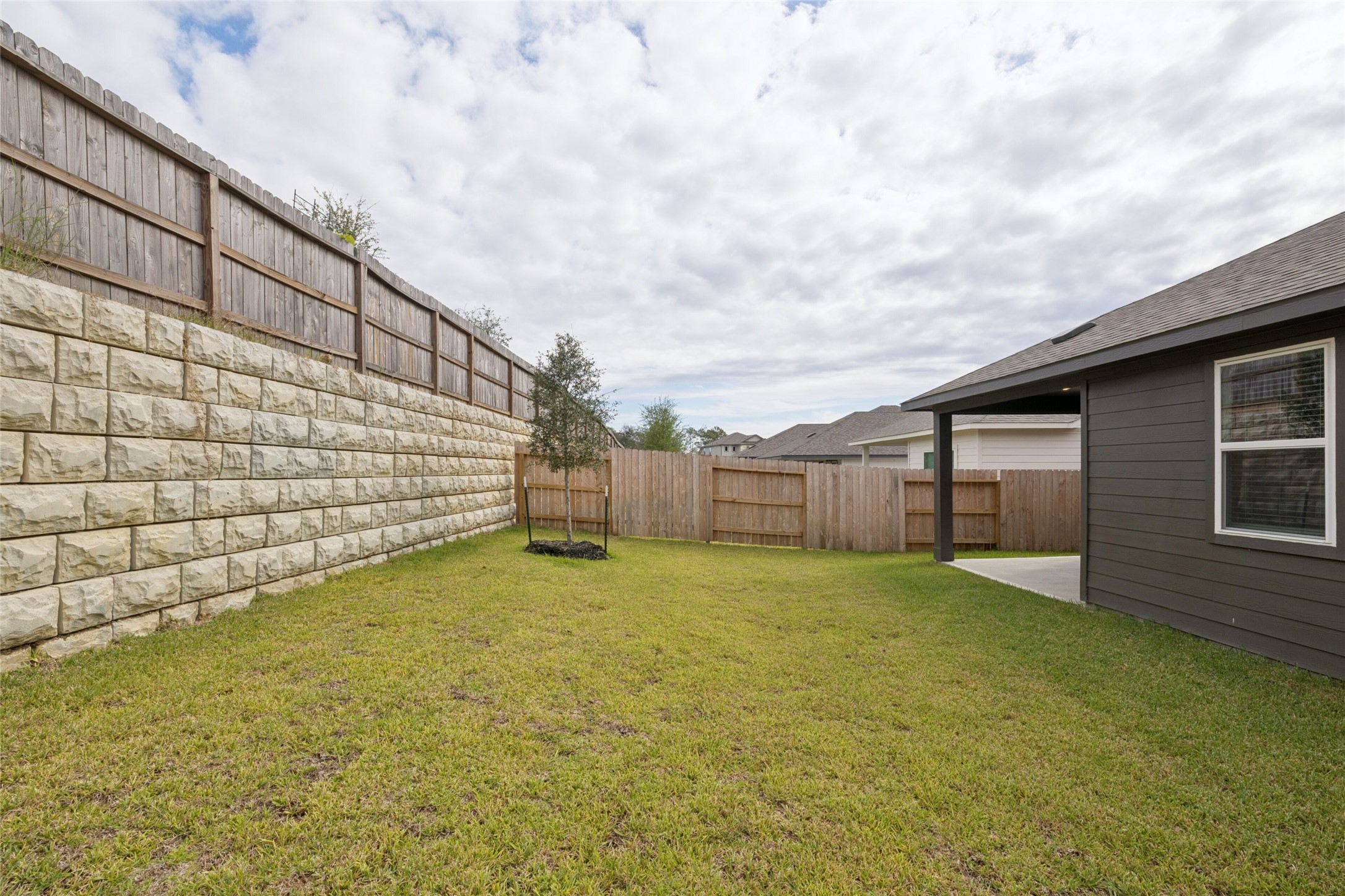 Spacious backyard with lush grass, privacy fencing, and a retaining wall, perfect for outdoor activities and relaxation.