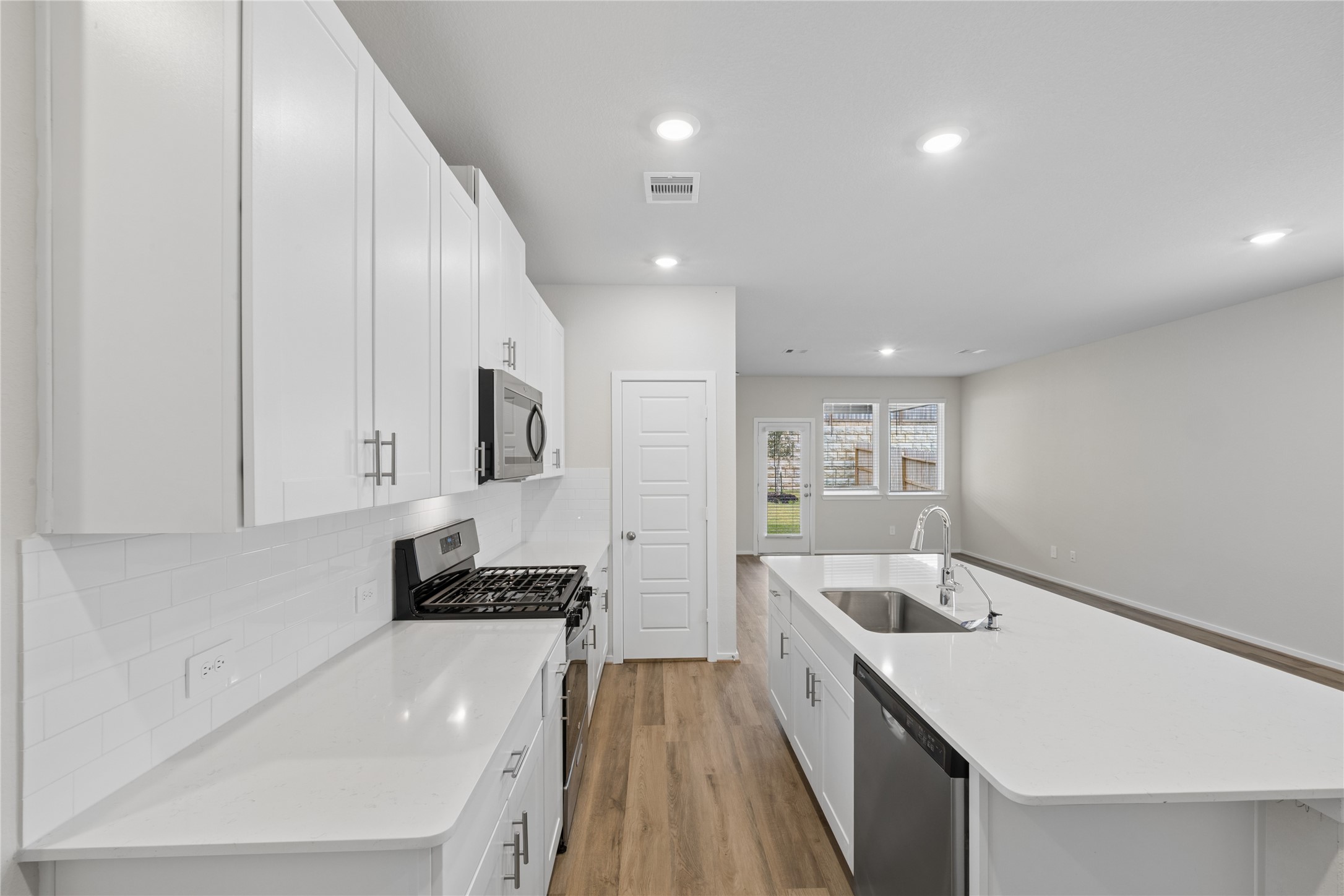 Modern kitchen featuring sleek white cabinetry, stainless steel appliances, and a spacious island with a sink, seamlessly leading into an open living area.