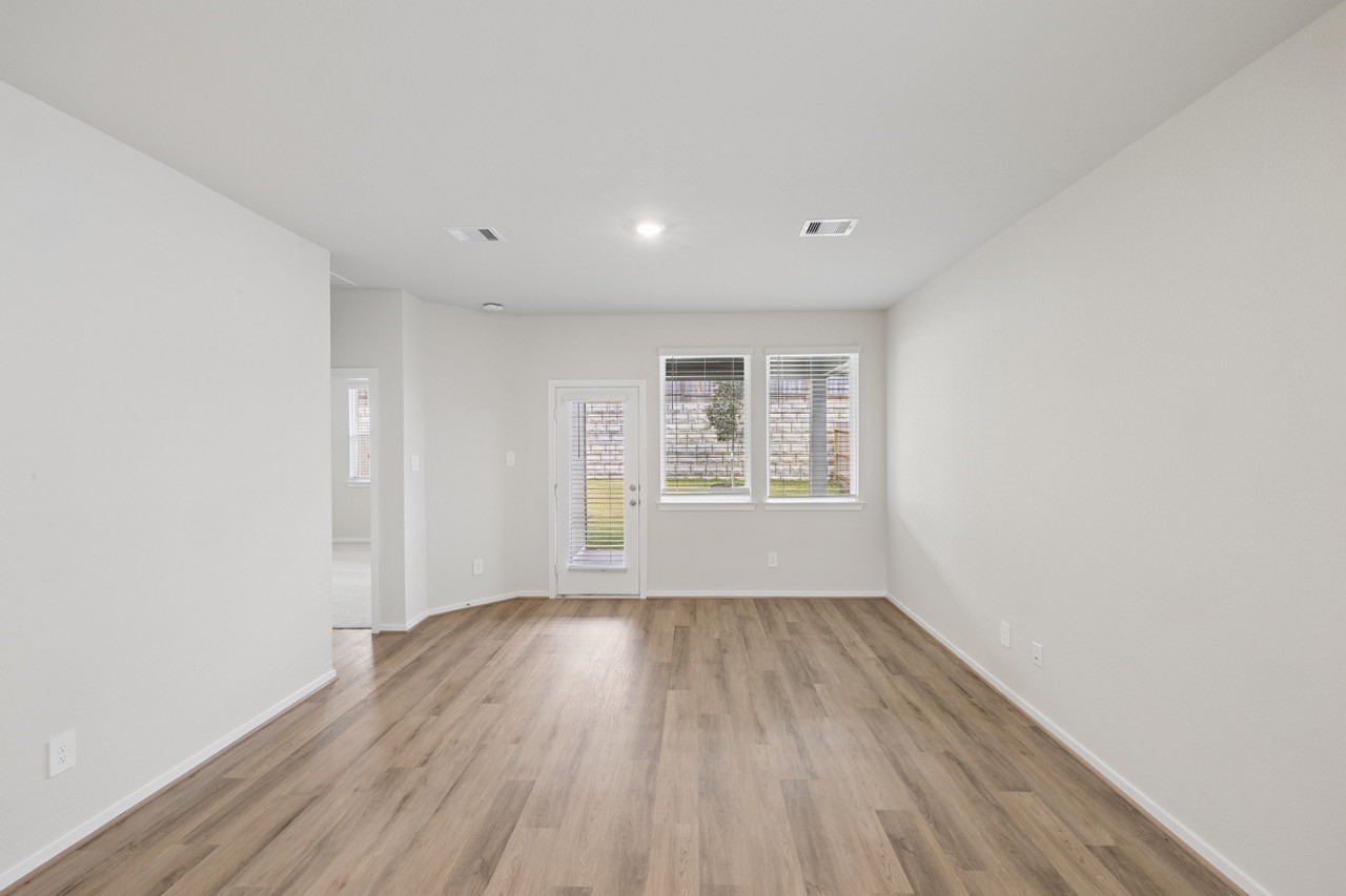 Bright and airy living space with sleek hardwood floors, large windows, and a door leading to the backyard, perfect for relaxing or entertaining.