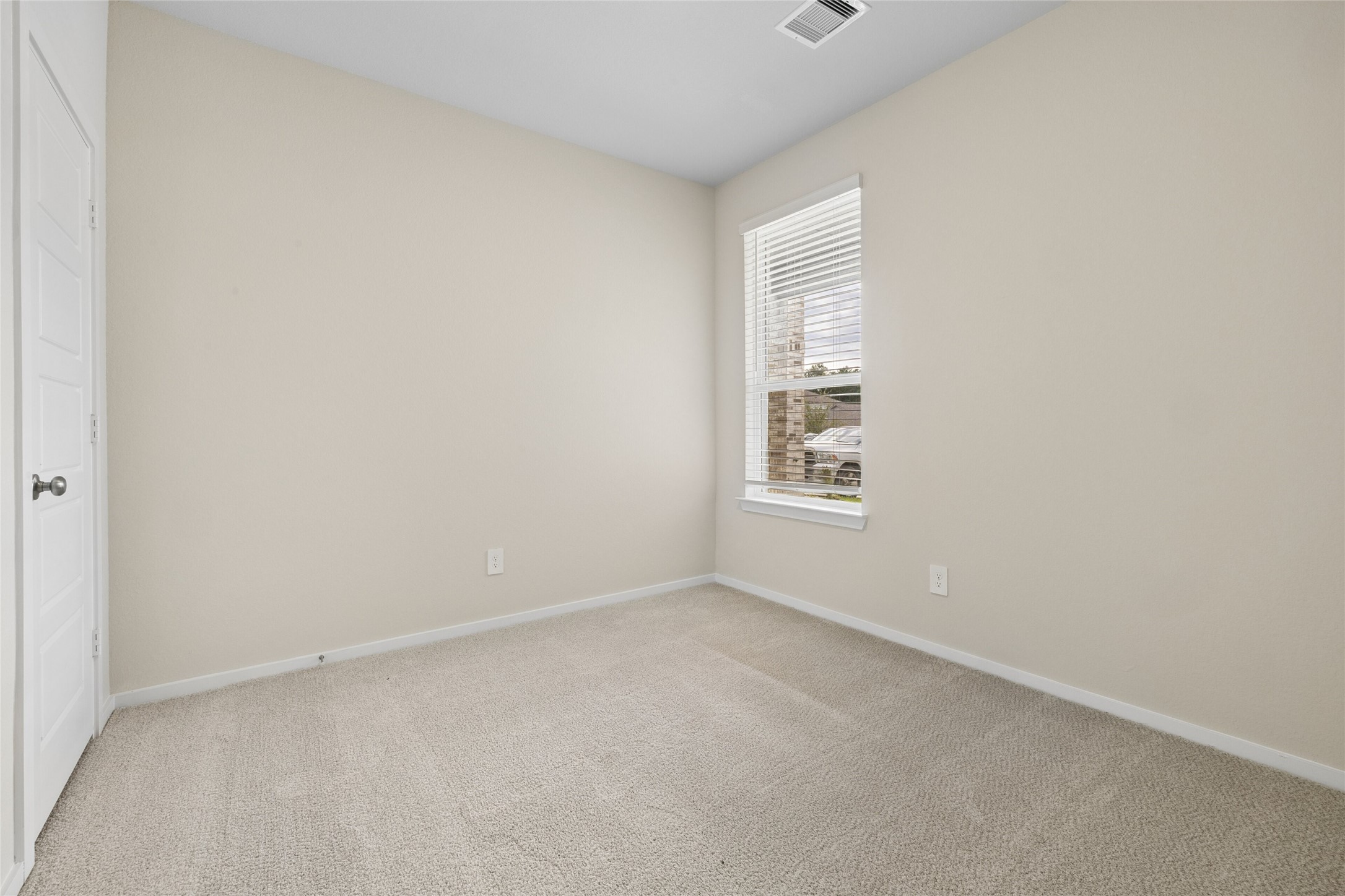 Cozy bedroom with soft carpet flooring, neutral walls, and a bright window allowing natural light to fill the space.