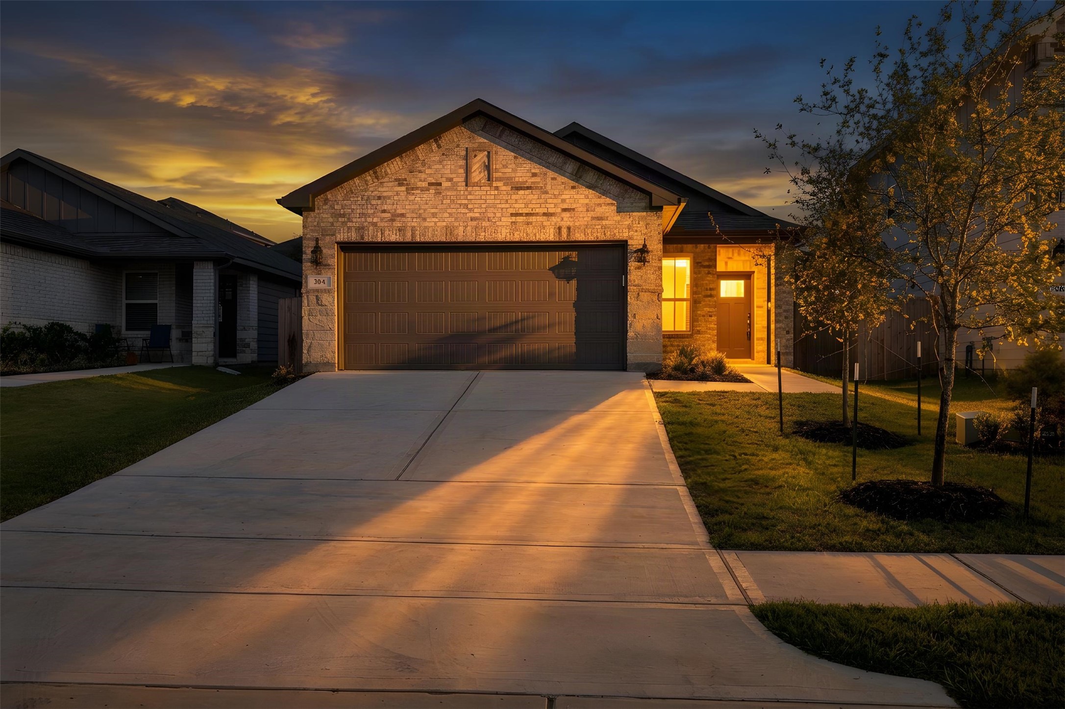 Charming single-story home with a welcoming facade, featuring a spacious driveway, a two-car garage, and a cozy front entrance illuminated by warm evening lights. Charming single-story home with a welcoming facade, featuring a spacious driveway, a two-car garage, and a cozy front entrance illuminated by warm evening lights.