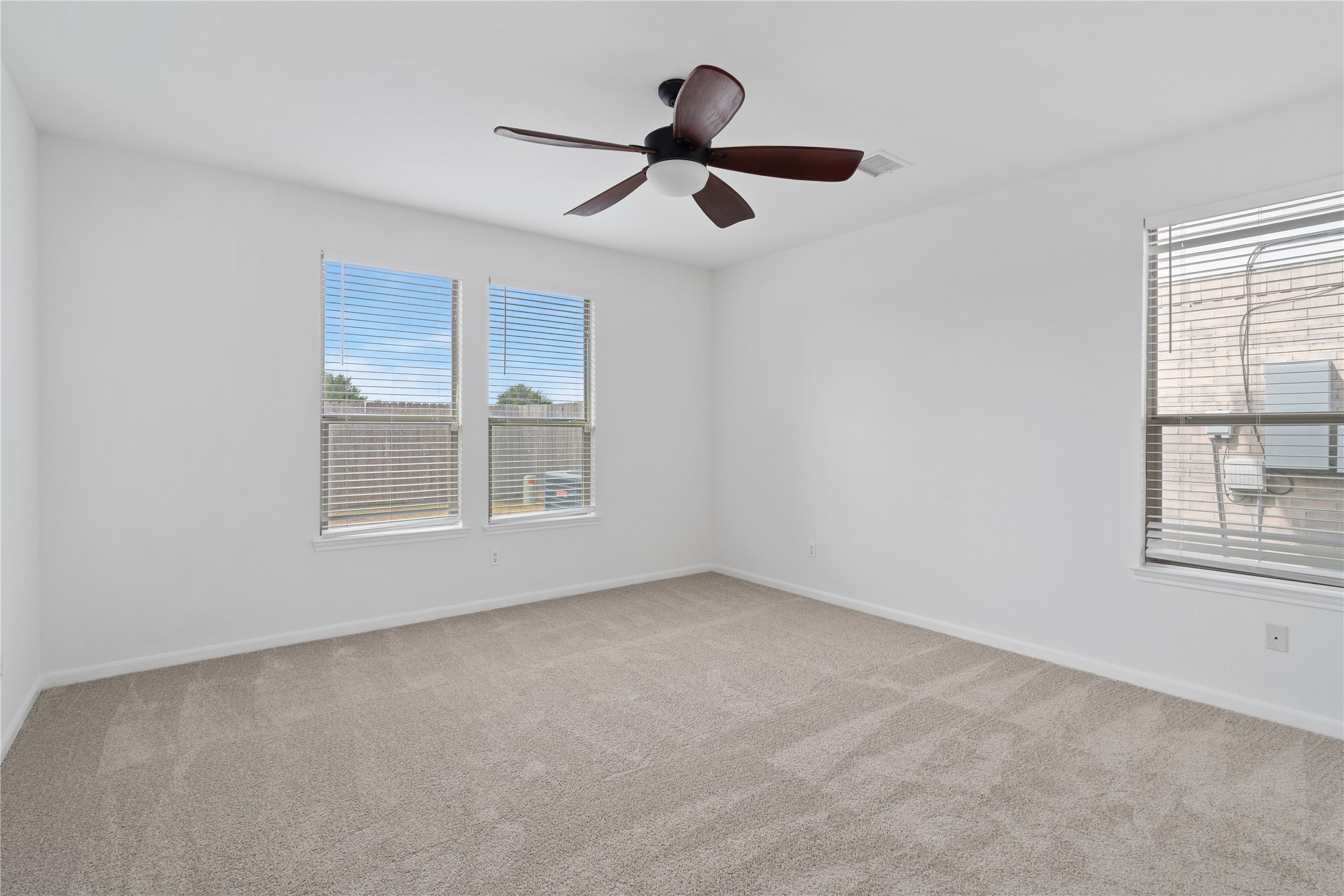 Bedroom  Spacious bedroom with neutral carpeting, a ceiling fan, and three windows that bring natural light into the room.