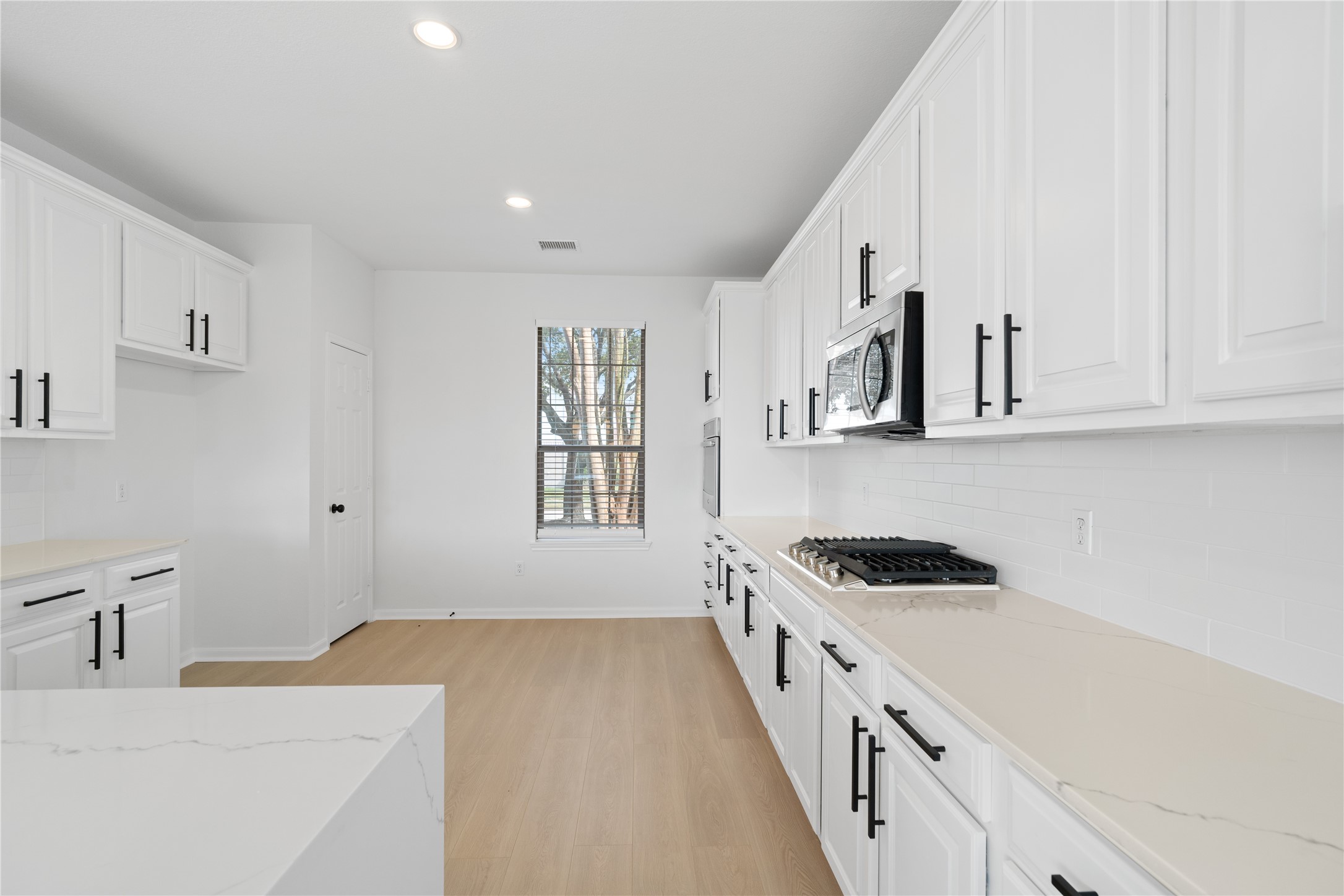 Kitchen Bright kitchen offers extensive white cabinetry with contrasting black hardware, stone-look countertops, subway-style tile backsplash, recessed lighting, and generous workspace. Kitchen Bright kitchen offers extensive white cabinetry with contrasting black hardware, stone-look countertops, subway-style tile backsplash, recessed lighting, and generous workspace.