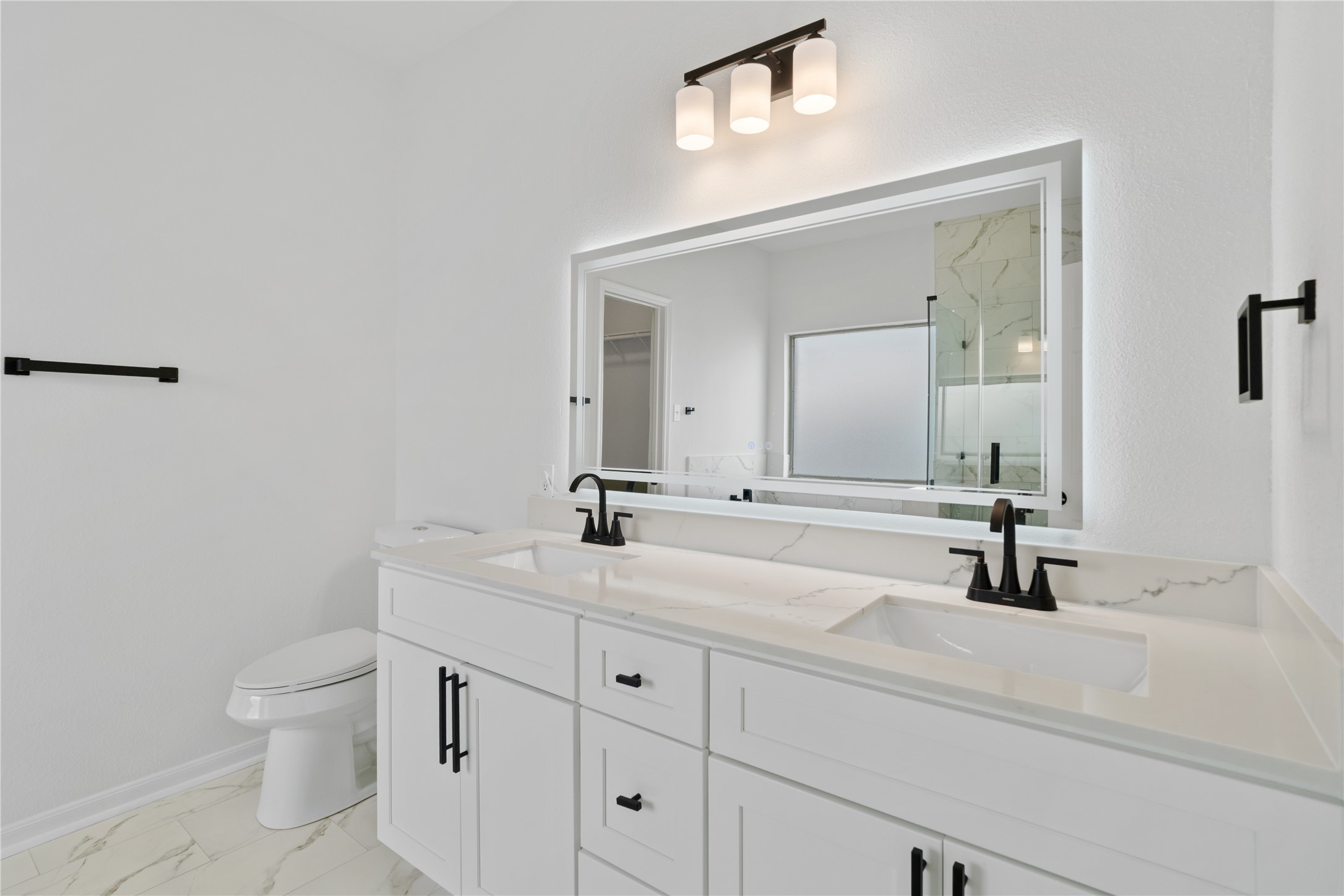 Primary Bathroom  Double-sink vanity offers abundant counter and cabinet space, complemented by matte-black fixtures and a large illuminated mirror.